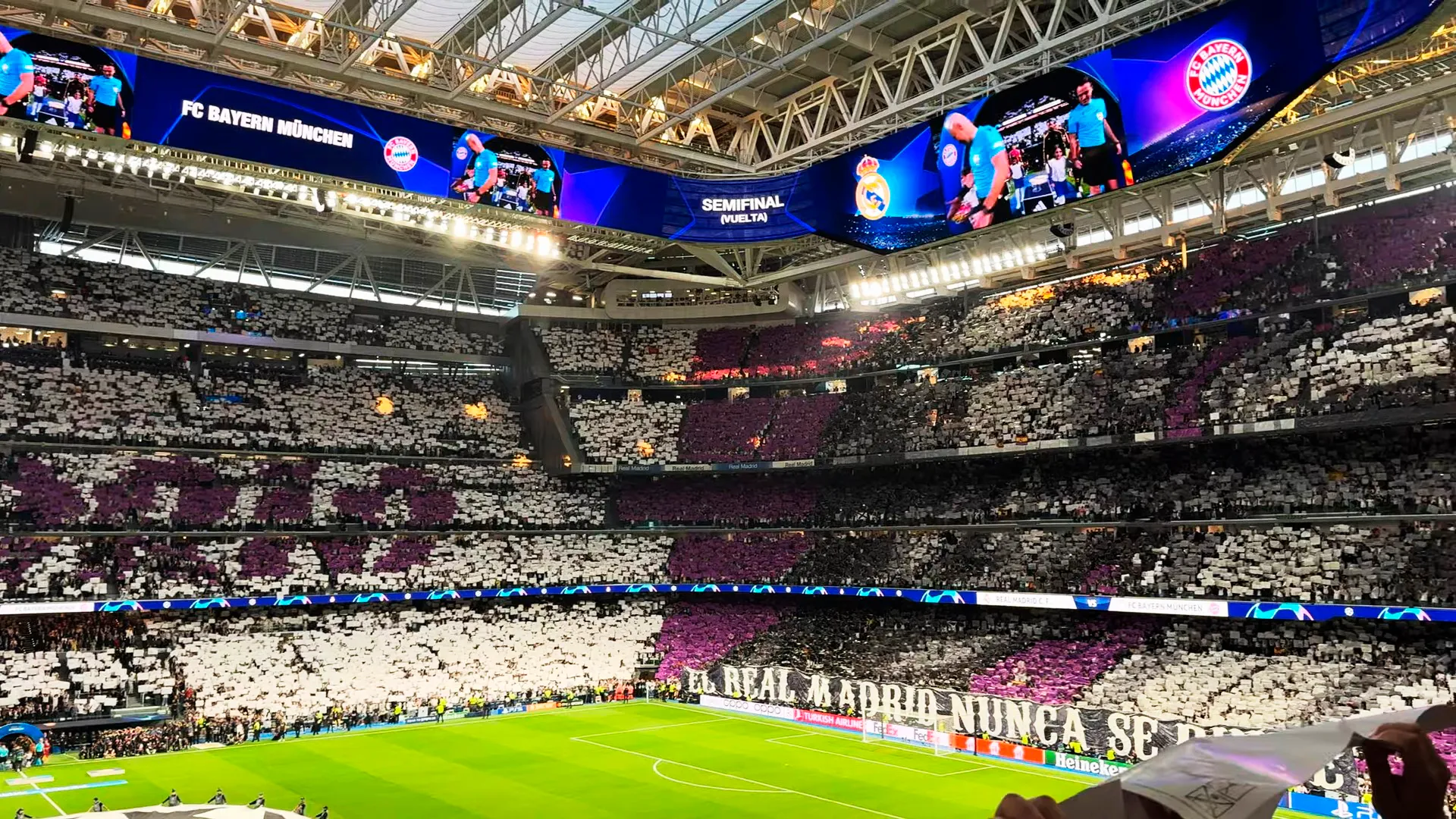 Wnętrze stadionu Santiago Bernabéu z wypełnionymi trybunami, zielonym boiskiem i dużymi ekranami cyfrowymi