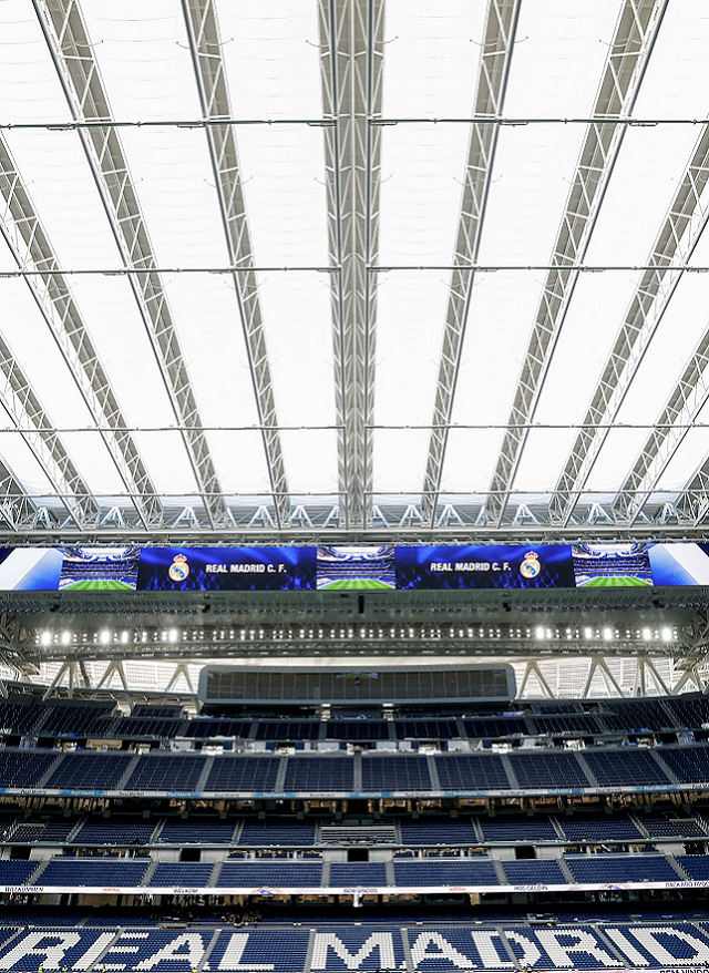 Wnętrze stadionu Santiago Bernabéu z niebieskimi siedzeniami i dużą konstrukcją dachu