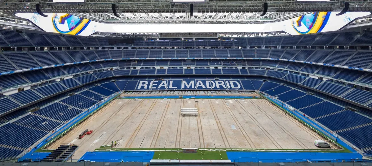 Wnętrze stadionu Santiago Bernabéu z niebieskimi siedzeniami, centralnym boiskiem i napisem „REAL MADRID”