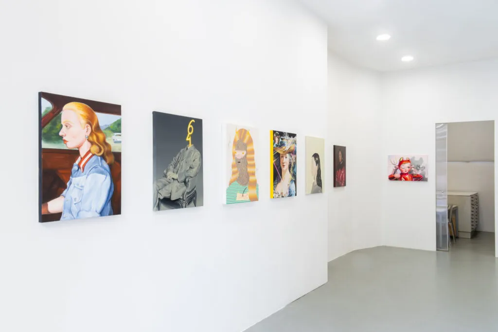 Paredes de galería blancas que exhiben una fila de coloridos retratos y obras de arte figurativo en un espacio de exposición luminoso con suelo gris
