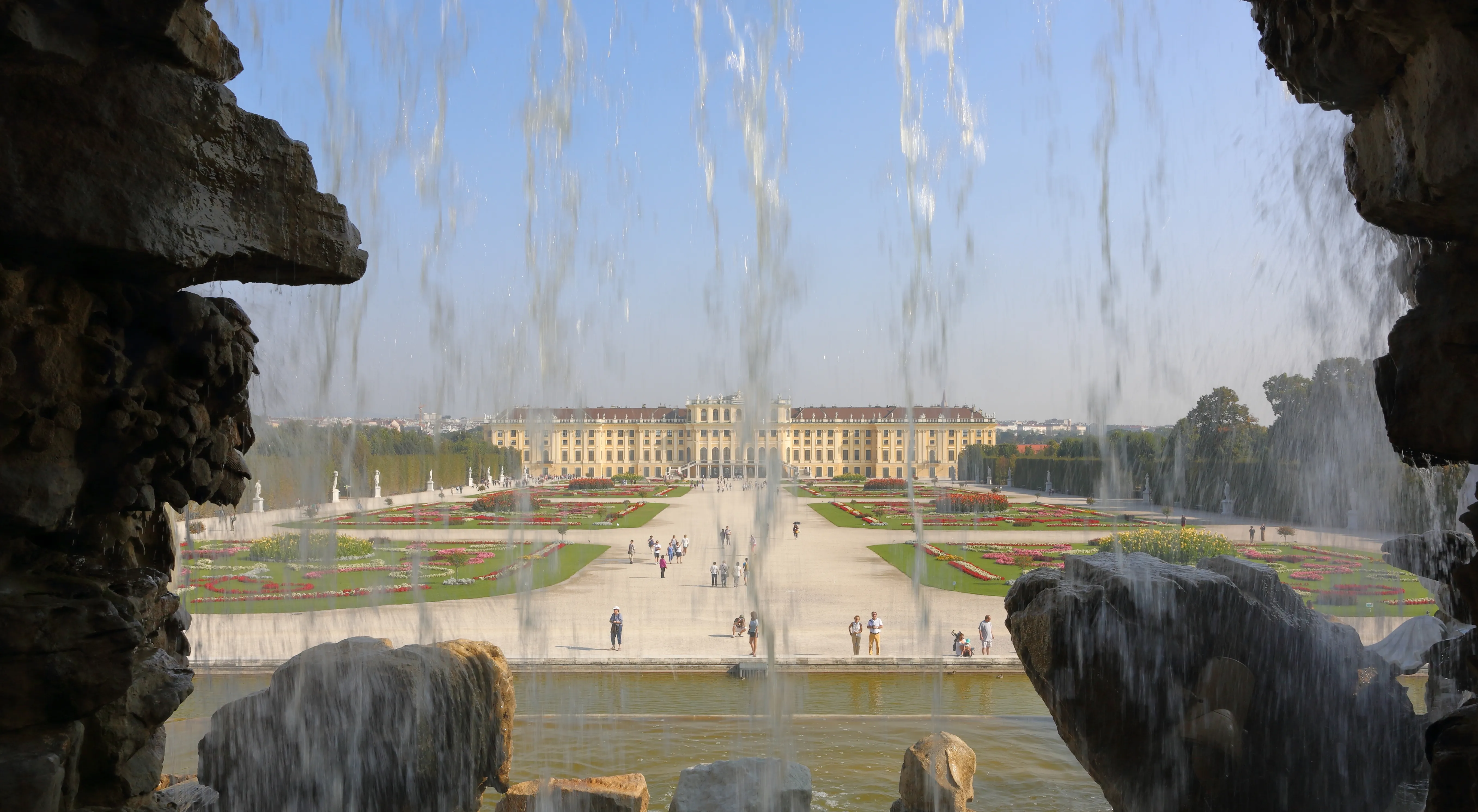Schönbrunn Palace seen through a stone fountain structure with water jets in the foreground
