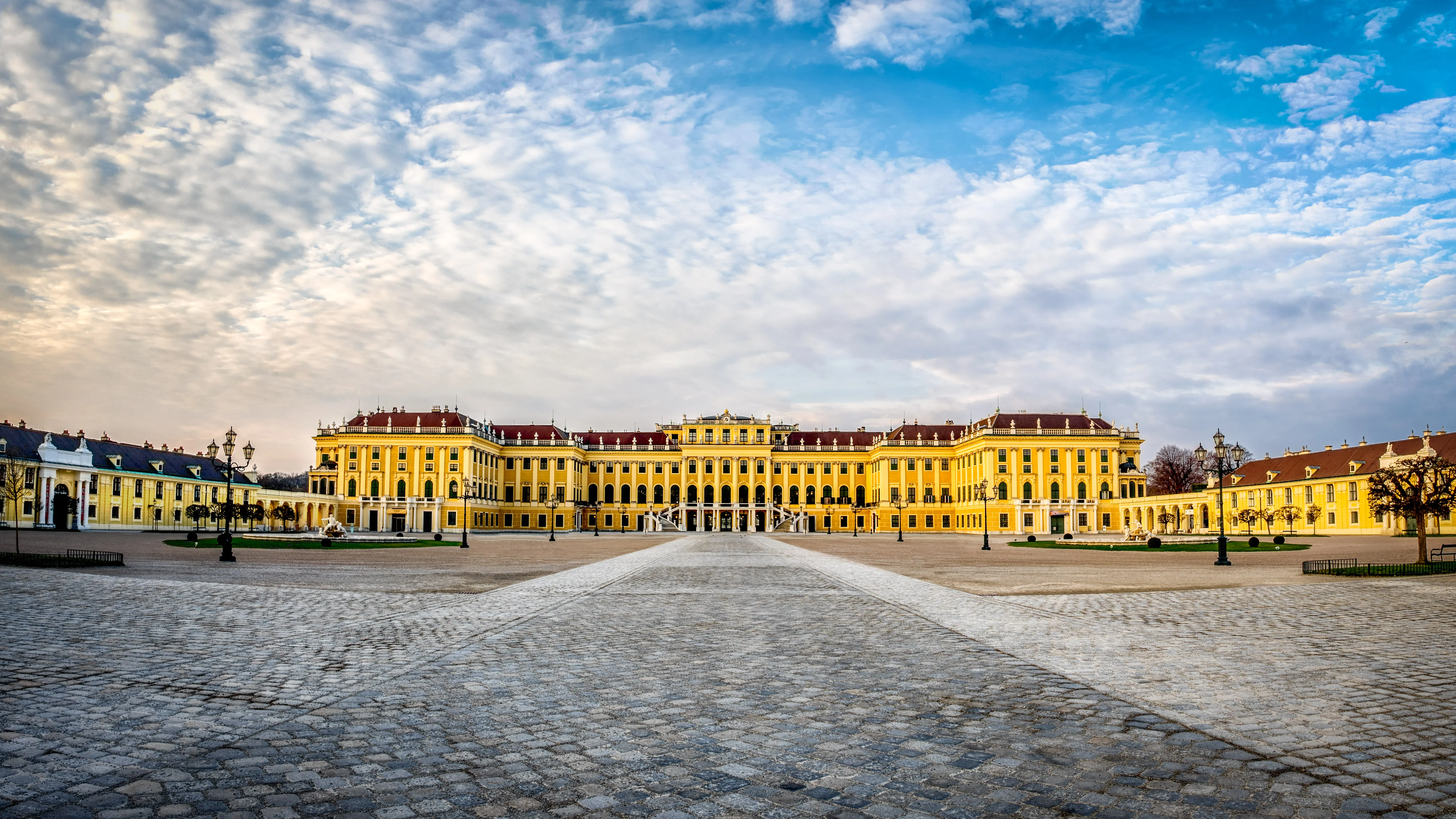 Schönbrunn Palace with a wide cobblestone courtyard and a bright blue sky with white clouds