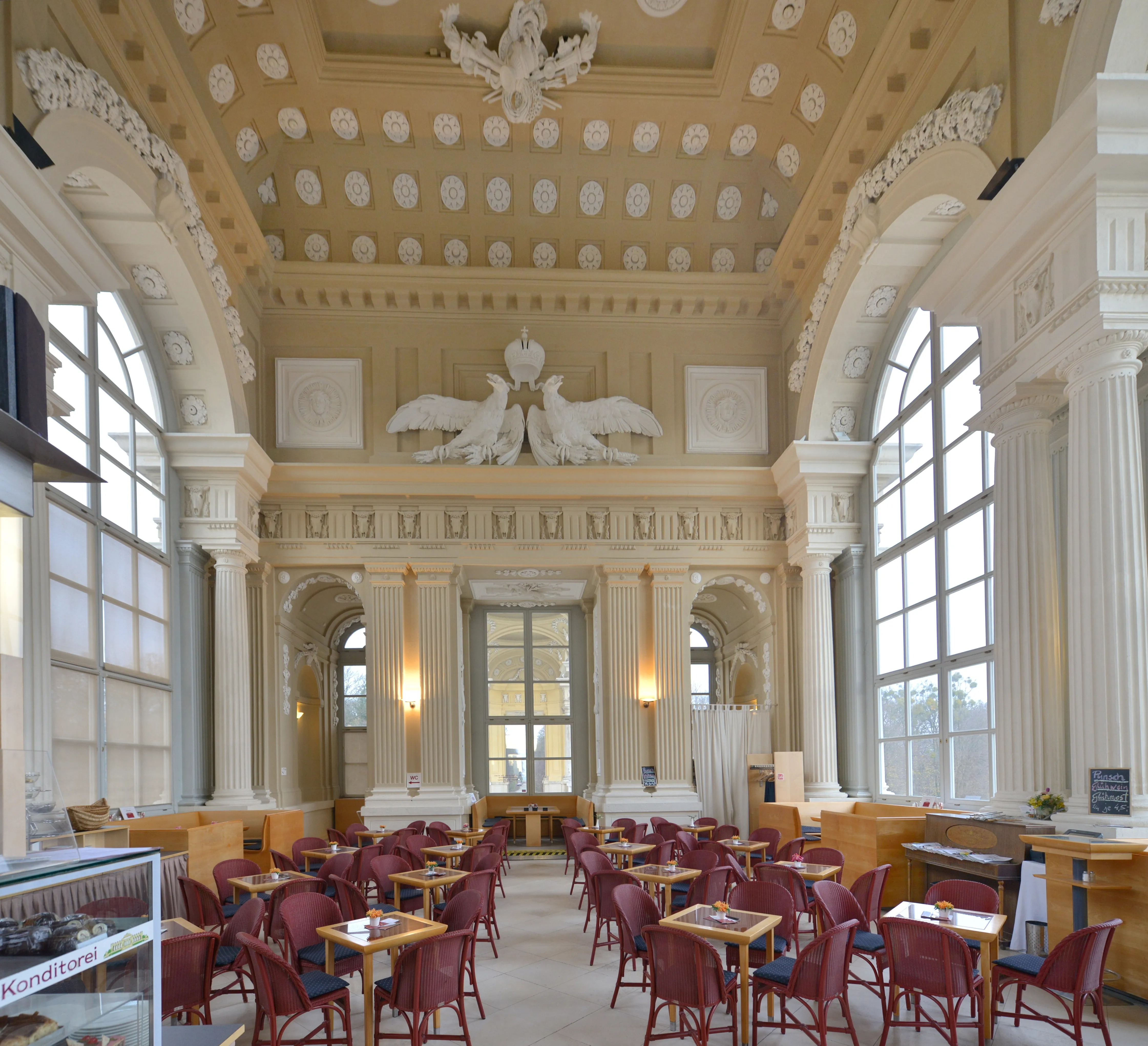 Ornate interior of a café with high ceiling, large windows, and tables and chairs