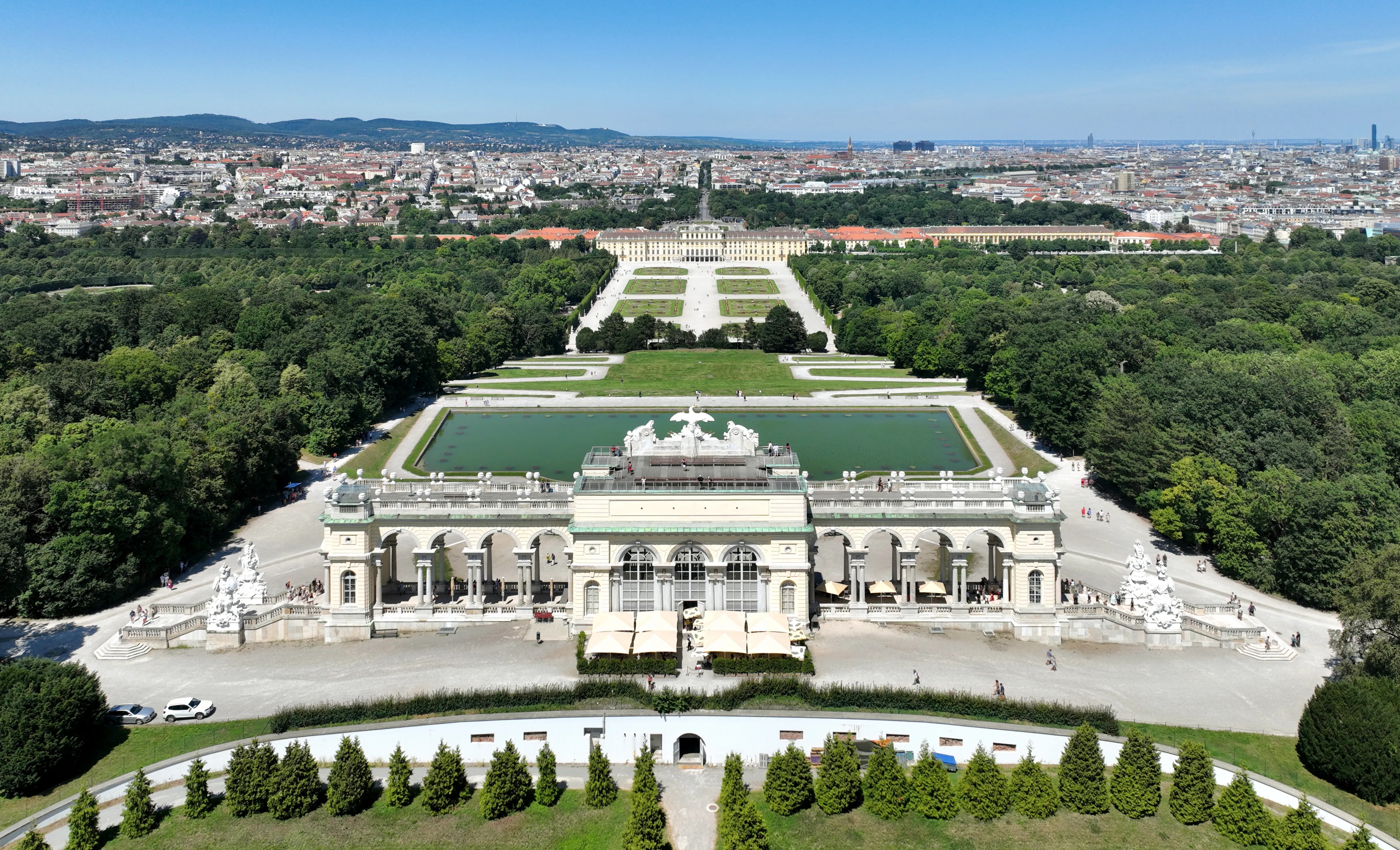 Aerial view of Schönbrunn Palace with its grand facade, central fountain, and formal gardens extending towards the city skyline.