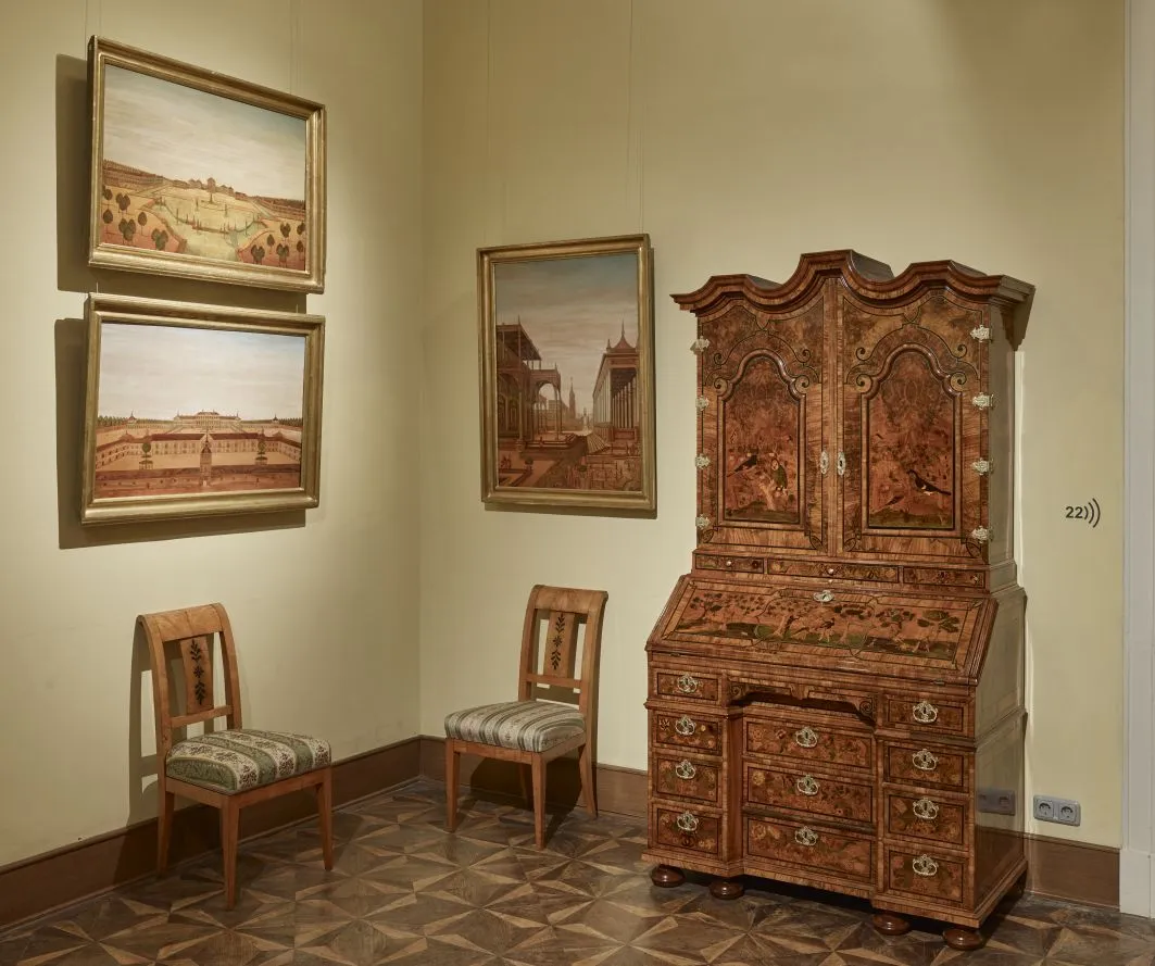 Een houten kabinet met ingewikkeld houtsnijwerk en schilderijen aan de muur in een museumgalerij