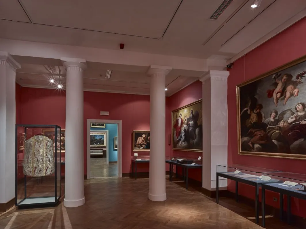 Interieur van het Schottenstift Museum met rode muren, witte zuilen en tentoongestelde schilderijen