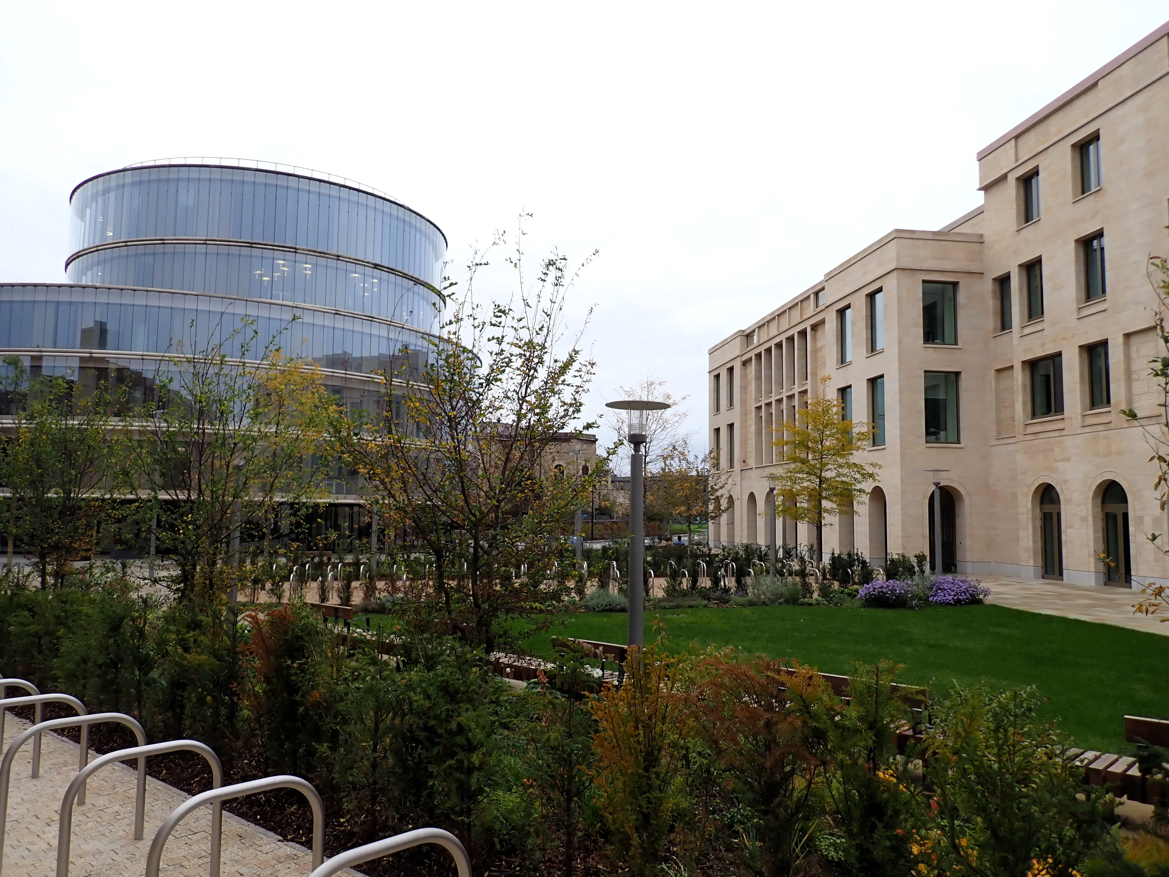 Exterior view of the Stephen A. Schwarzman Centre for the Humanities showing a circular glass building next to a stone building with a green courtyard garden
