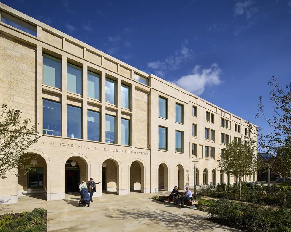 Stone facade of the Stephen A. Schwarzman Centre for the Humanities with arched entrance, large windows, and people in the courtyard under a blue sky