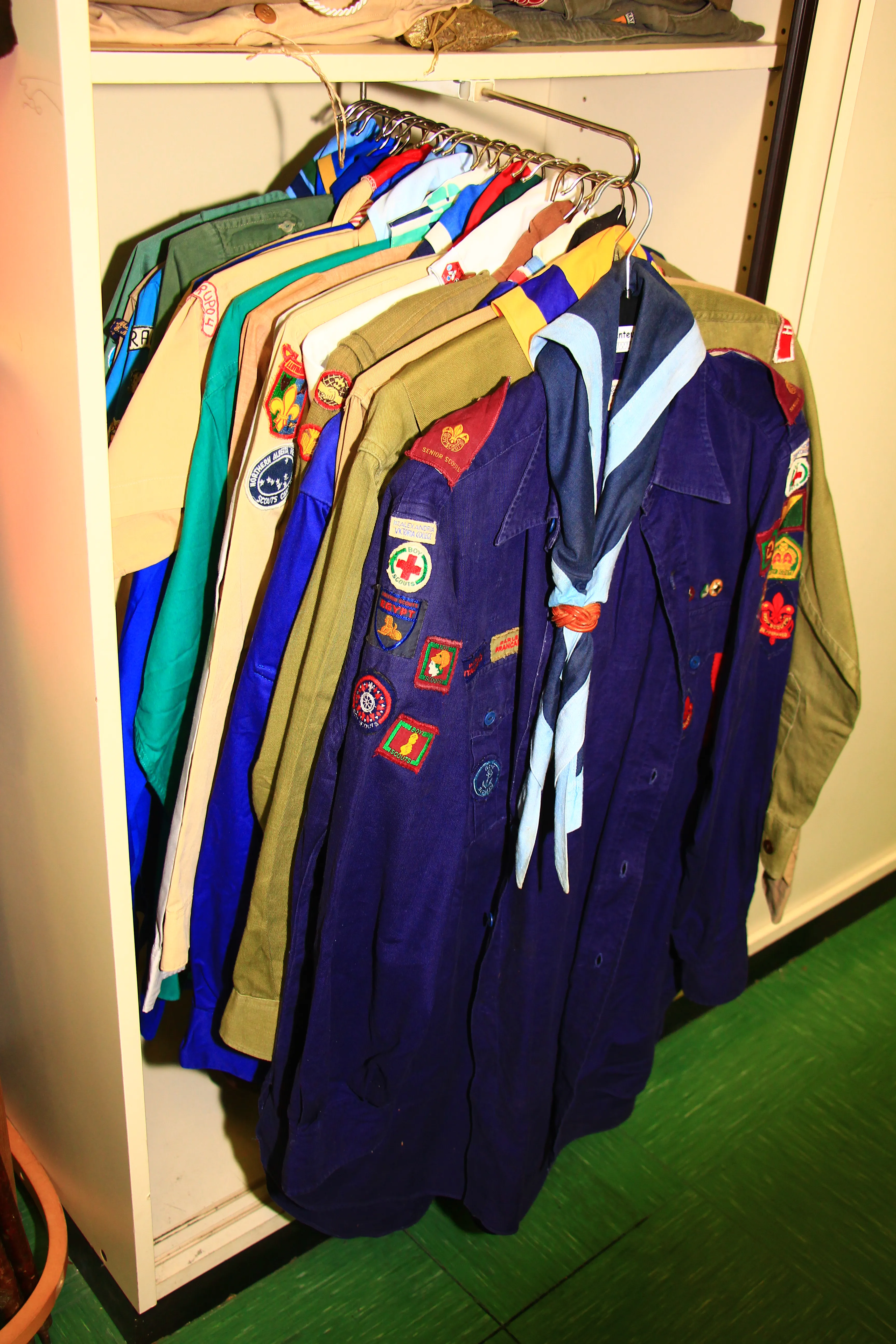 Scouting uniforms with patches and neckerchiefs hanging on a rack in a museum display