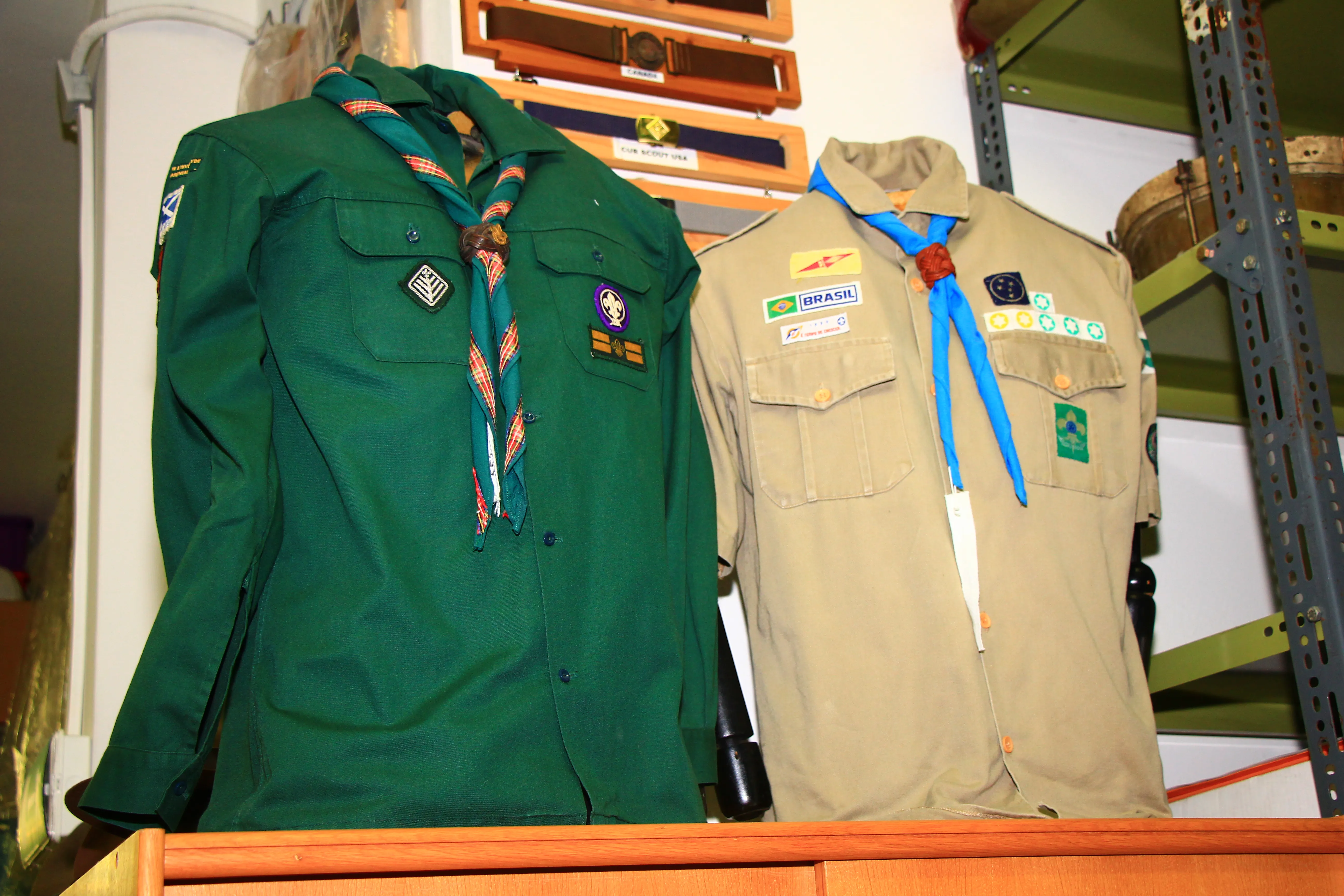Two scout uniforms with badges and neckerchiefs displayed on a wooden surface