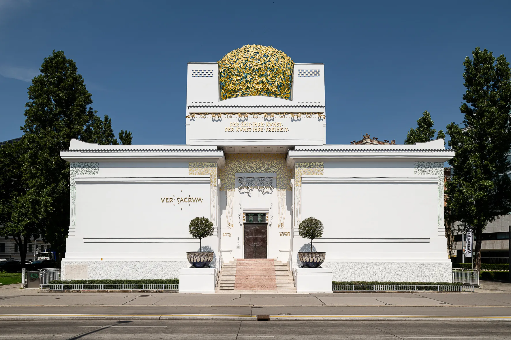 White art nouveau building with a golden dome and 'VER SACRUM' inscription under a clear blue sky