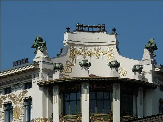The Vienna Secession building with gold decorative patterns and green sculptures on a white facade under a blue sky