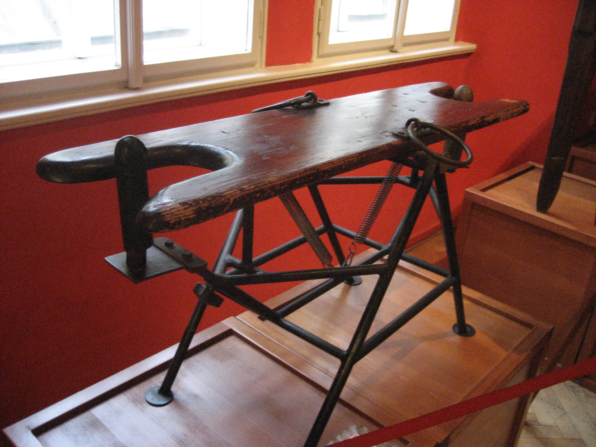 Een houten en metalen mechanisch apparaat tentoongesteld in een museum met rode muren en een raam.