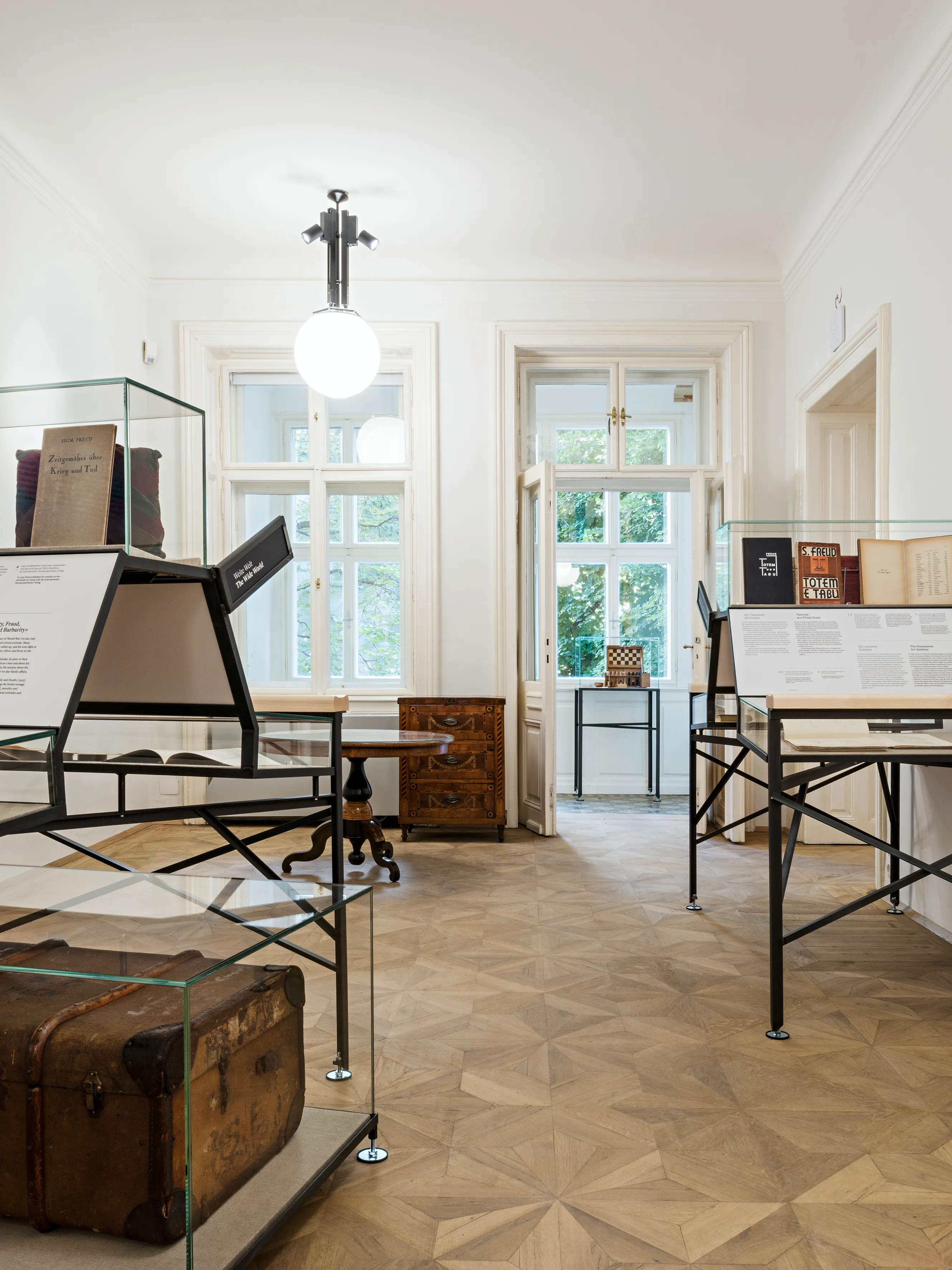 interieur van een museumzaal met vitrines, een vintage koffer en grote ramen