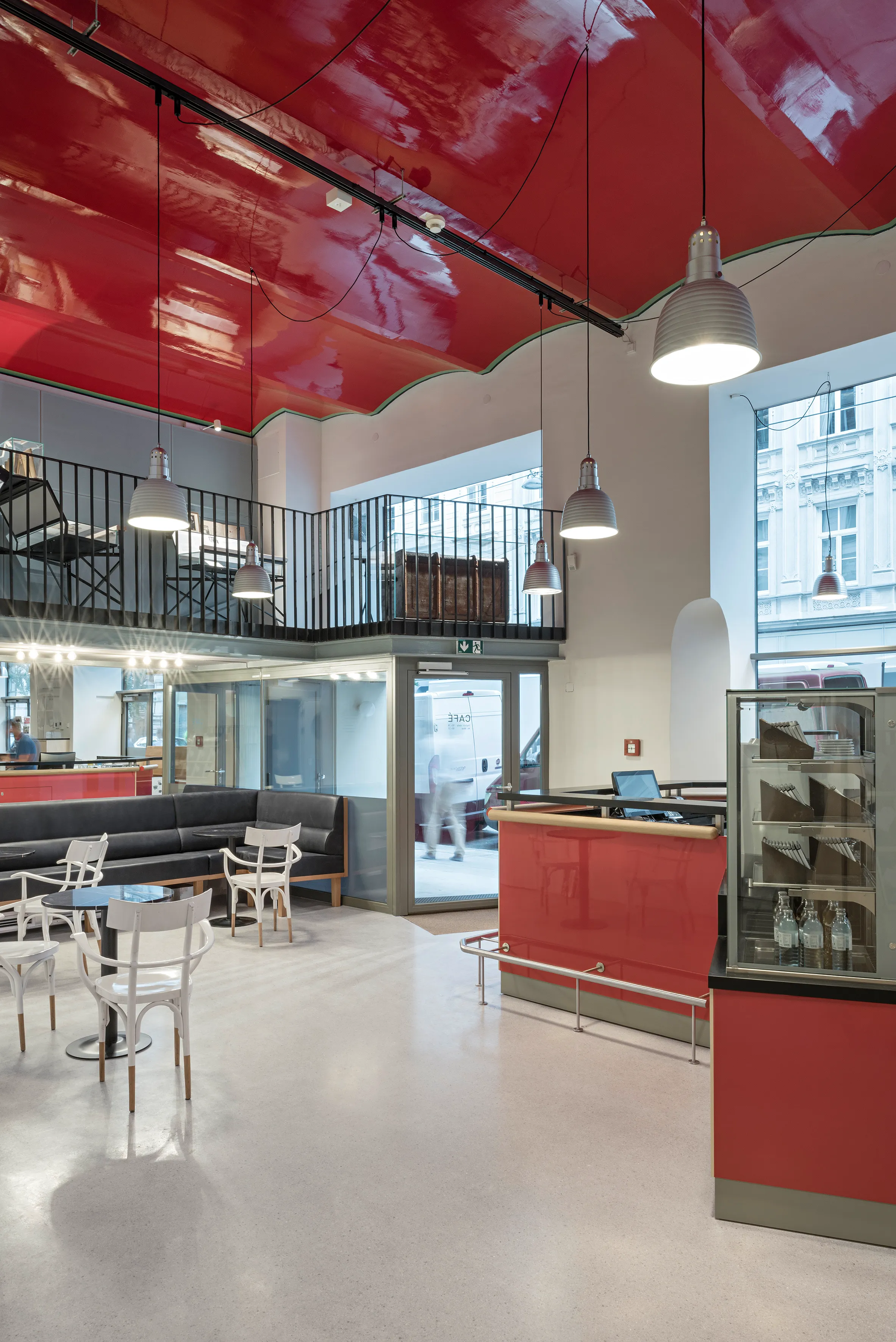 Interieur van een museum met een rood plafond, witte stoelen en een rode balie