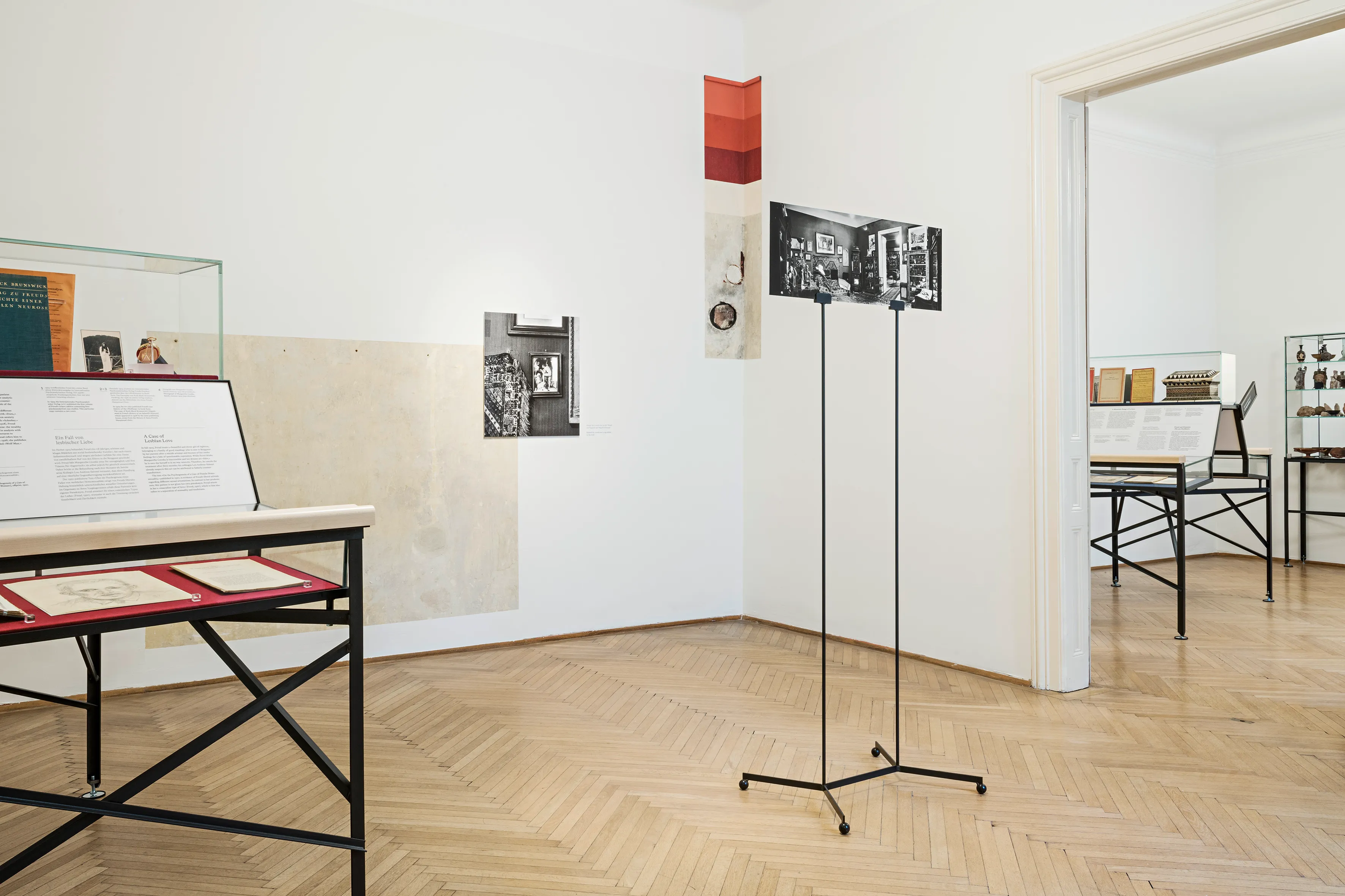 expositieruimte met vitrinekast, vrijstaande fotostandaard en ingelijste afbeeldingen aan witte muren