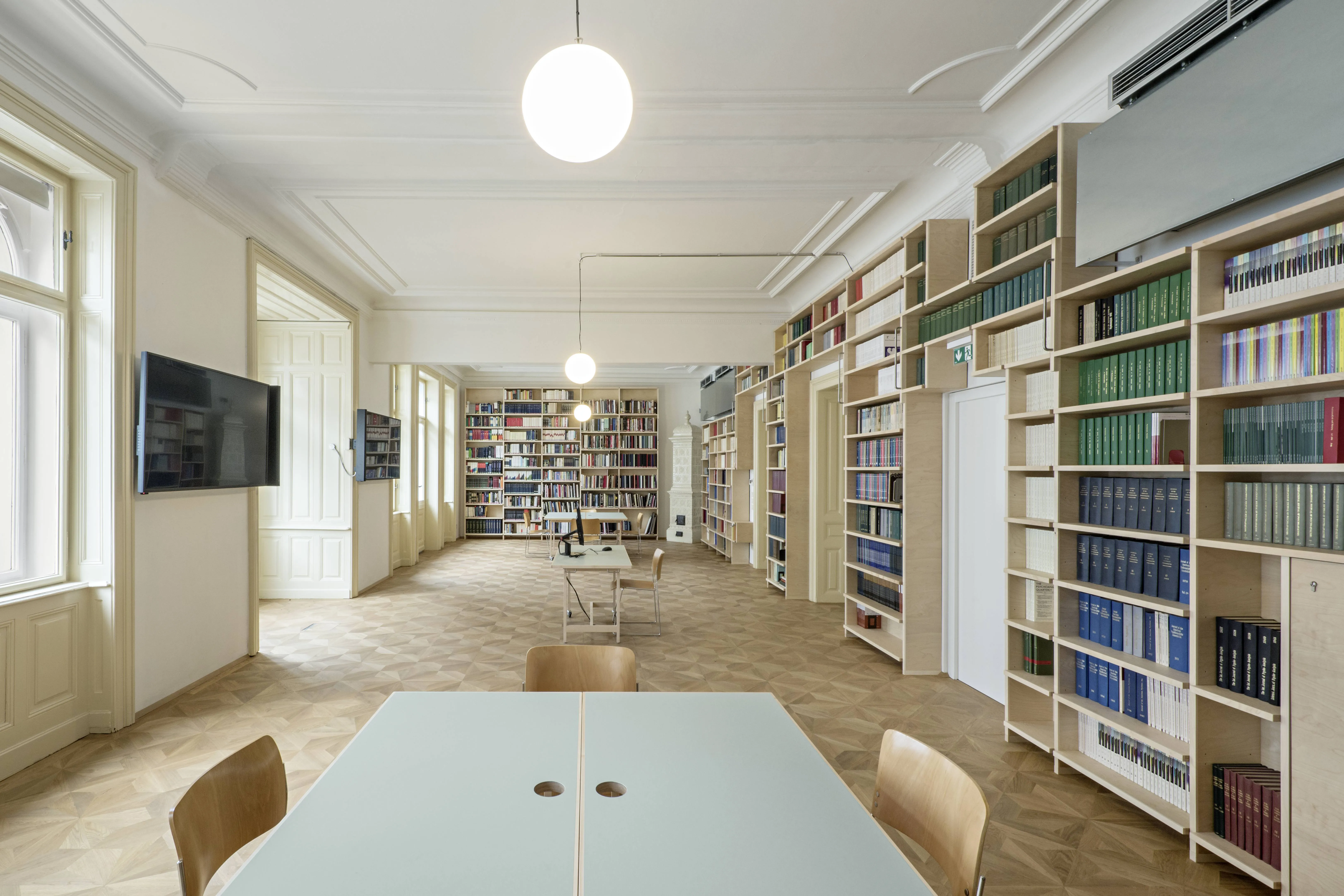 lange leeskamer met boekenplanken, tafels, stoelen en grote ramen