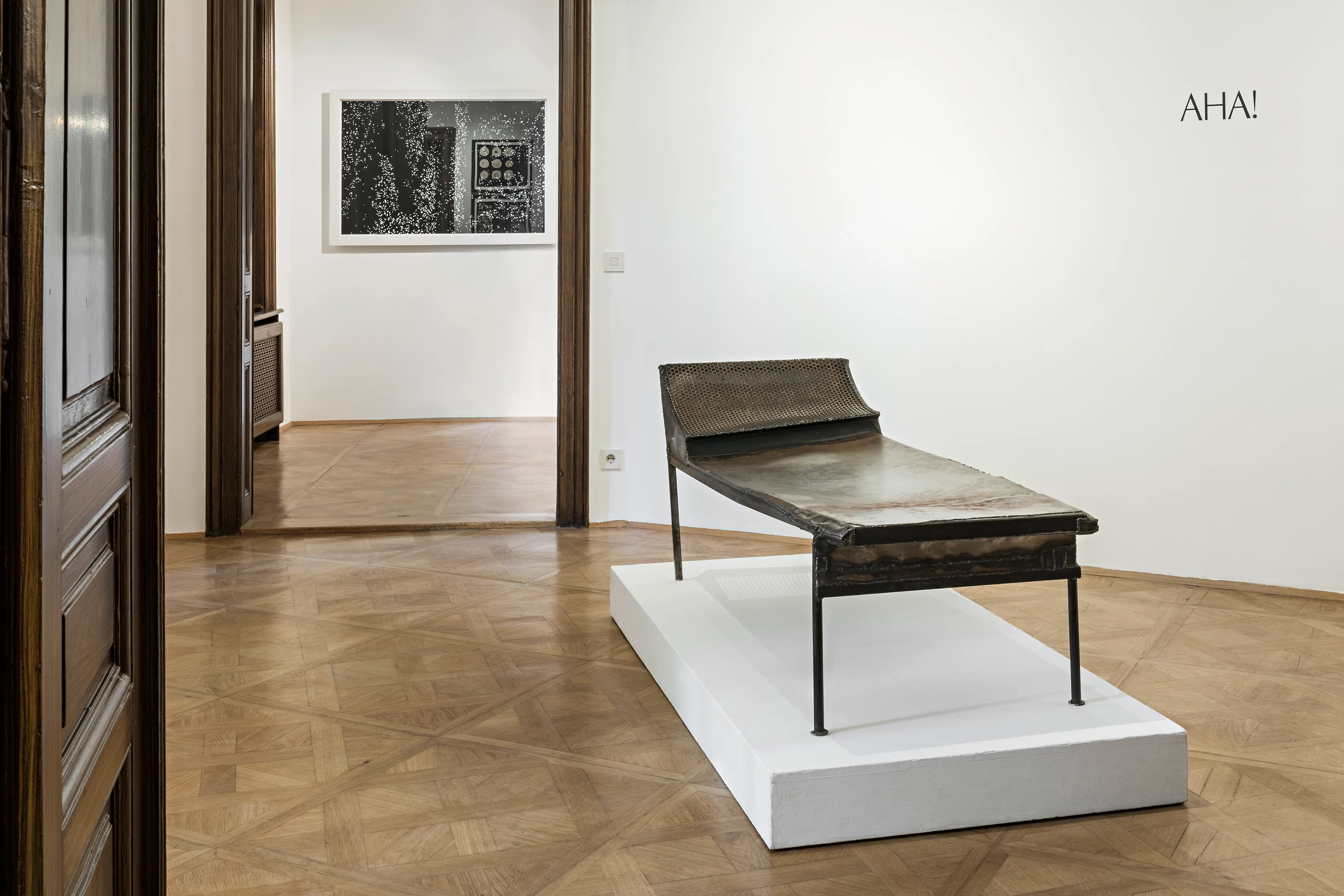psychoanalytische divan op een wit voetstuk in een museumgalerij met een ingelijste foto aan de muur