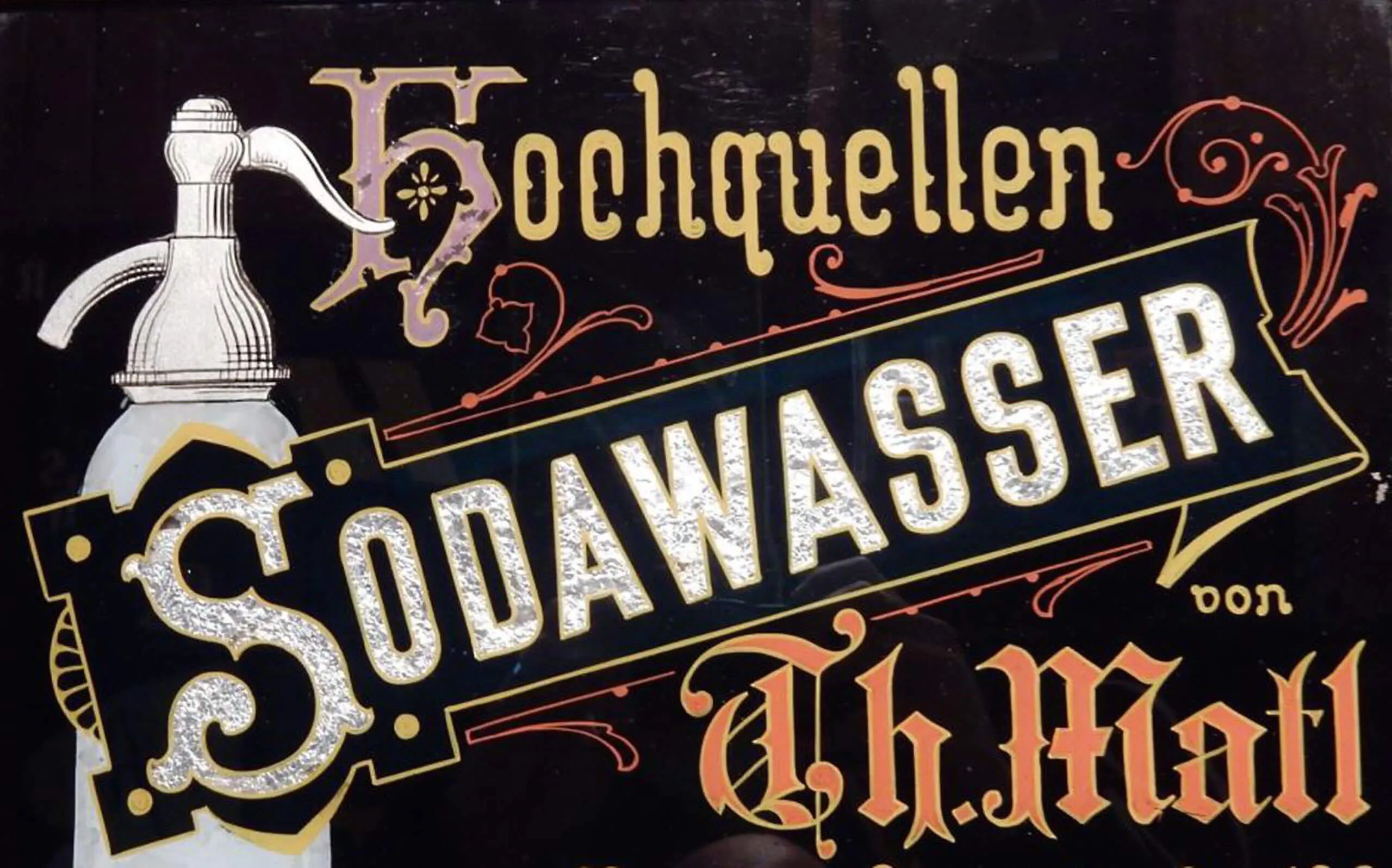 Un letrero antiguo pintado a mano con letras ornamentadas que dice 'Hochquellen SODAWASSER von Th. Mall' y una ilustración de una botella de seltz.