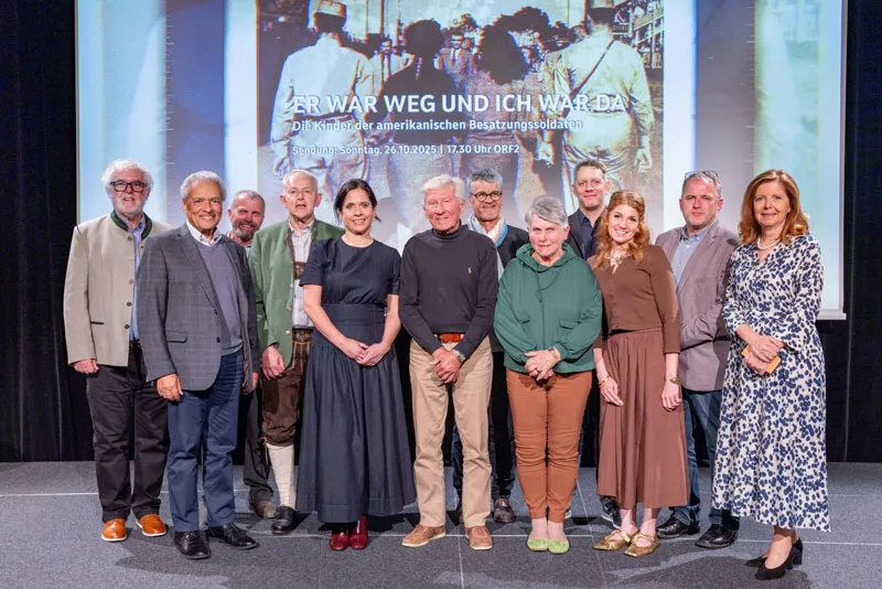 Group of people standing on a stage in front of a screen with a historical photo and text