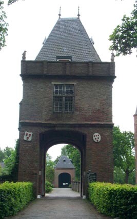 Brick gatehouse with gabled roof and arched passage leading to Slot Zuylen castle, flanked by manicured hedges and heraldic shields