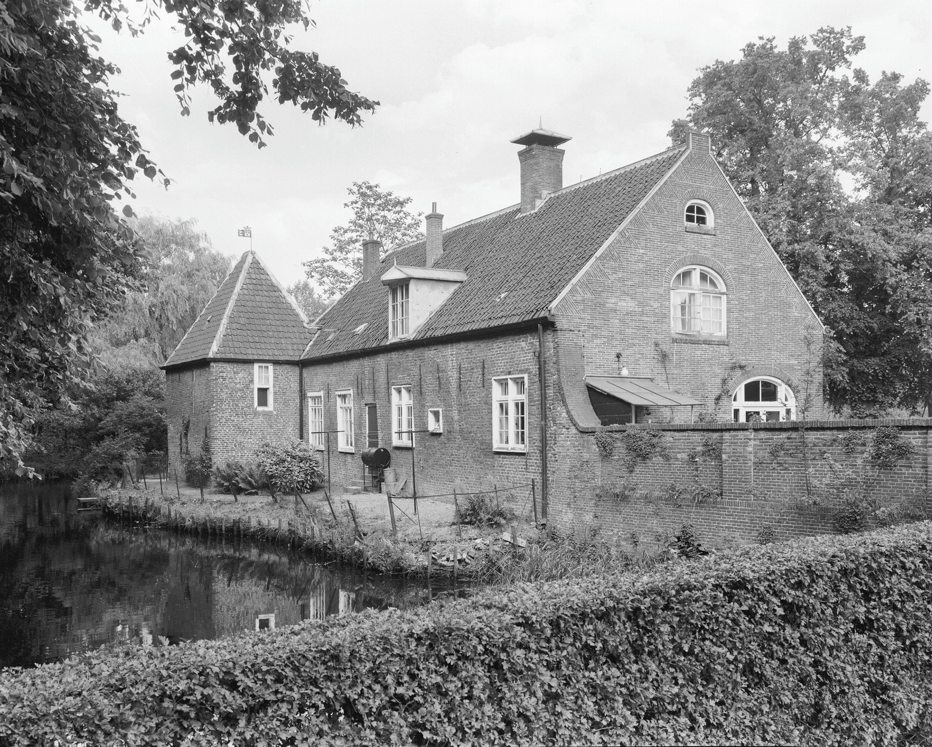 Historic brick building of Slot Zuylen with moat, hedges, and trees in black and white