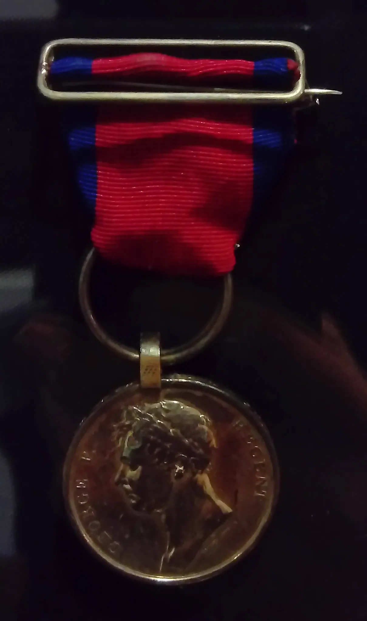 Primer plano de una medalla de bronce con una cinta roja y azul, con un retrato de perfil de un hombre.