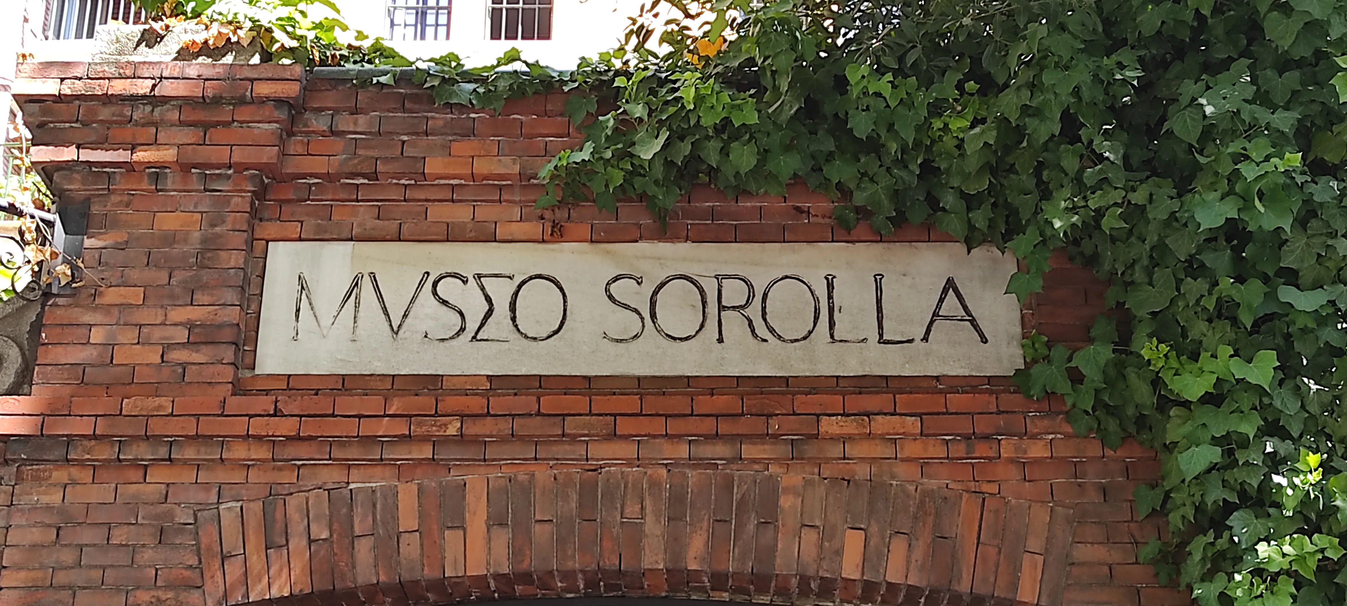 Stenen bord met 'MVSSEO SOROLLA' op een bakstenen muur met klimop
