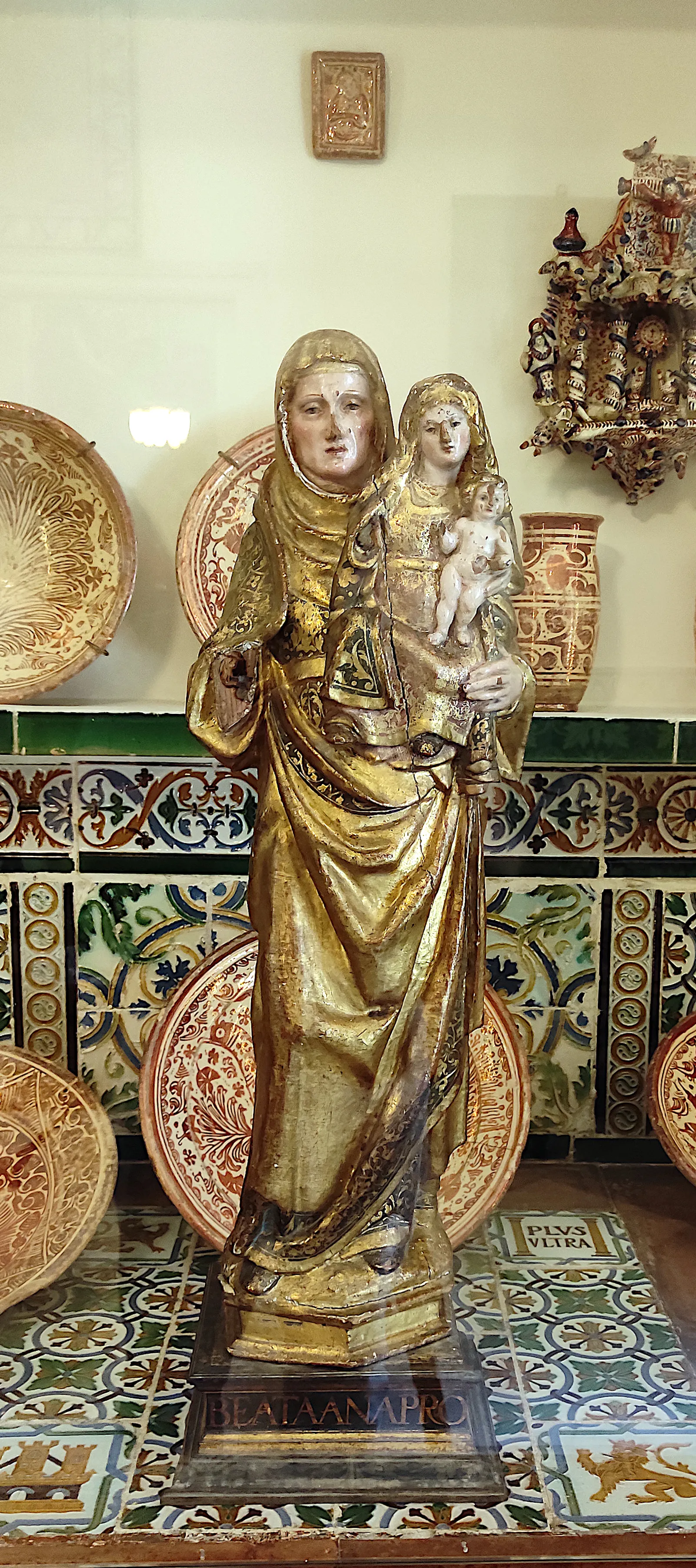 Estatua dorada de la Virgen María sosteniendo al Niño Jesús, rodeada de coloridos platos y azulejos de cerámica