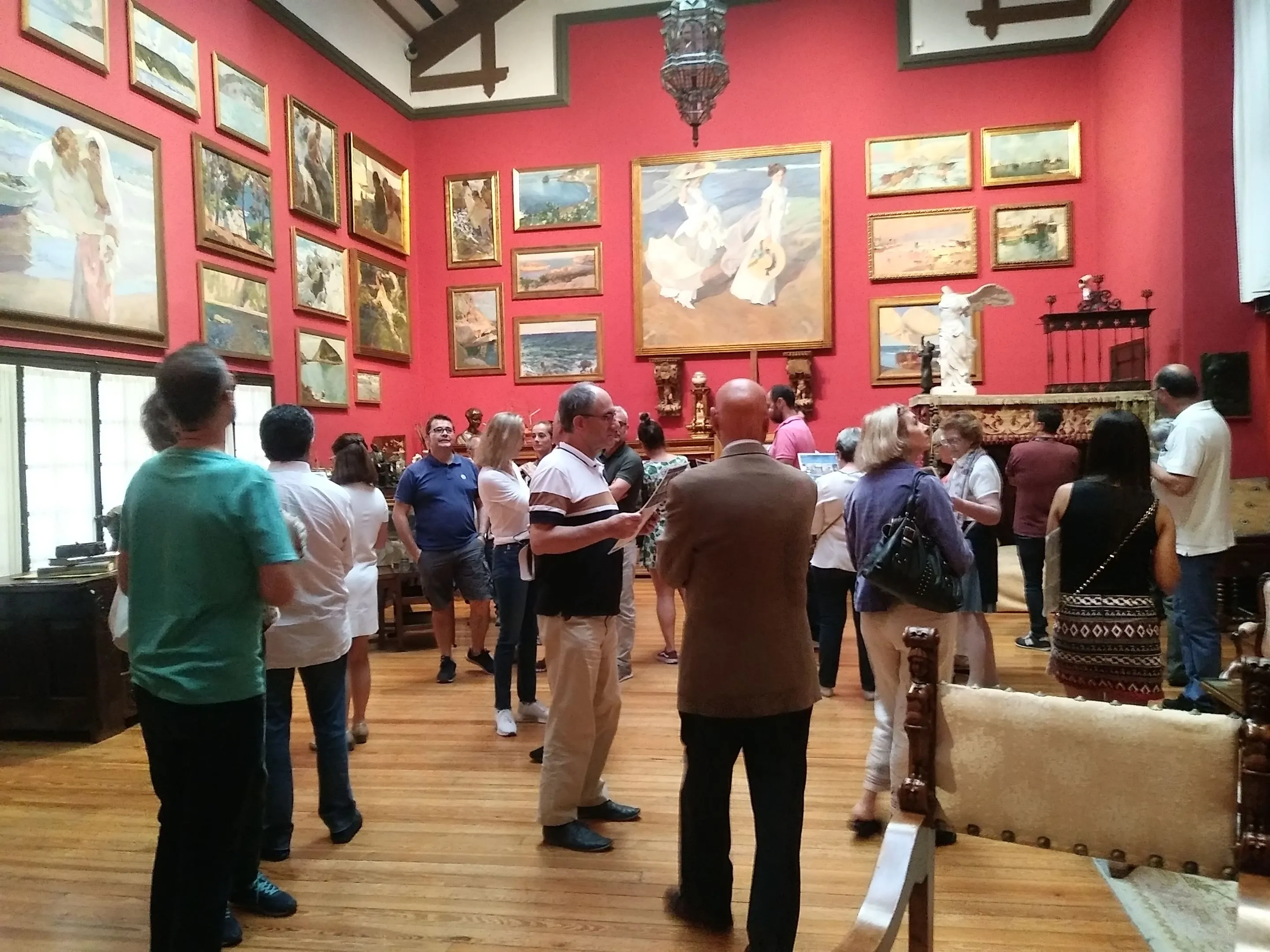 Personas viendo pinturas en una galería con paredes rojas y suelos de madera
