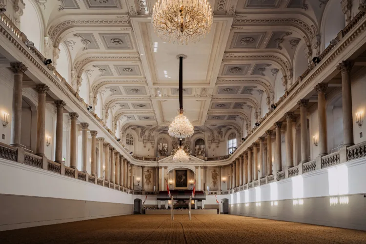 Ornate interior of a grand hall with high ceilings, chandeliers, columns, and a long central space.