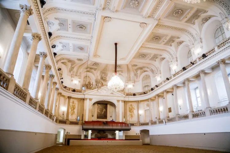 Grand baroque hall with white columns, ornate ceiling, and chandelier