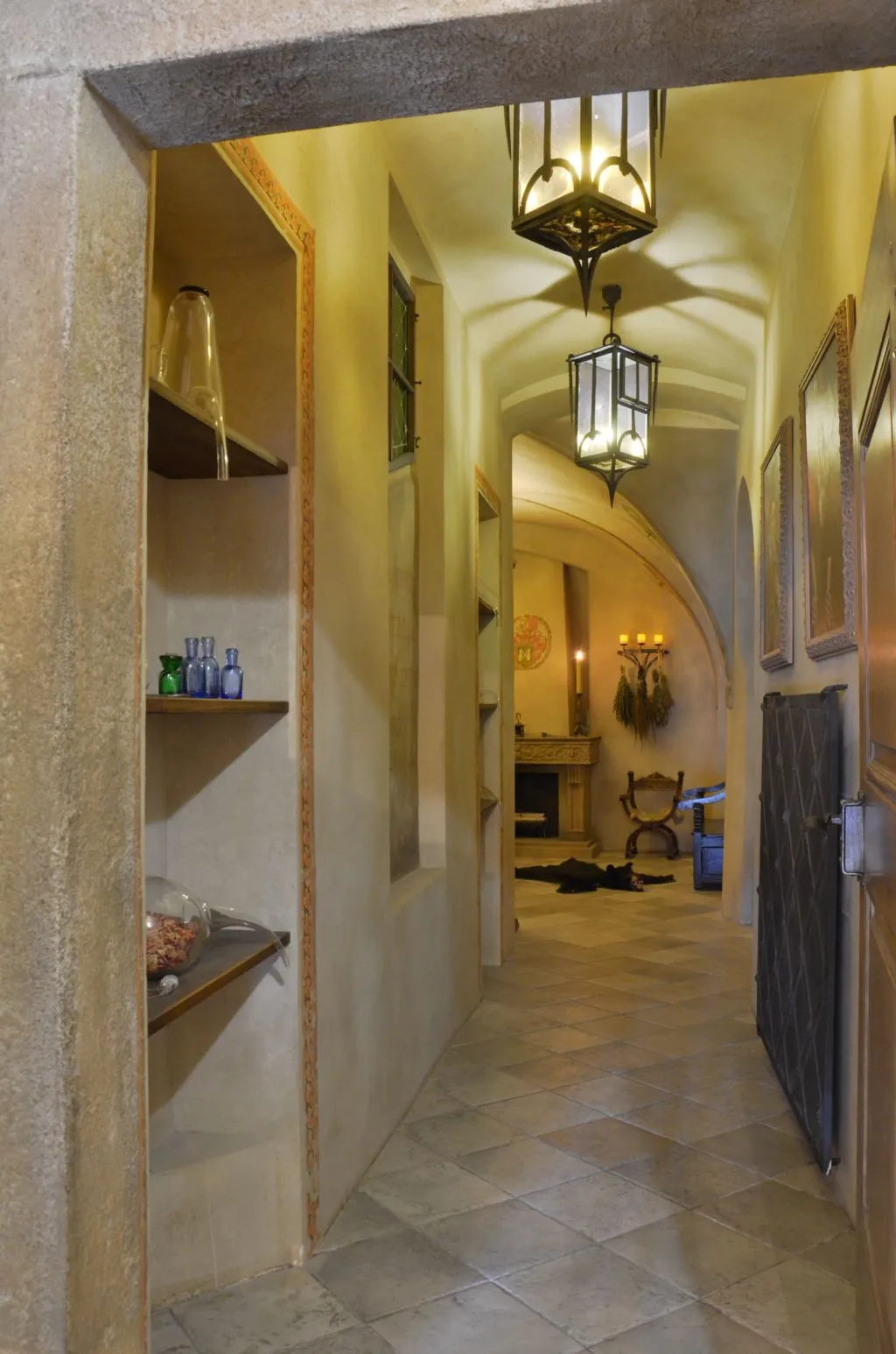 stone hallway with arched ceiling, hanging lanterns, and shelves with glass vessels
