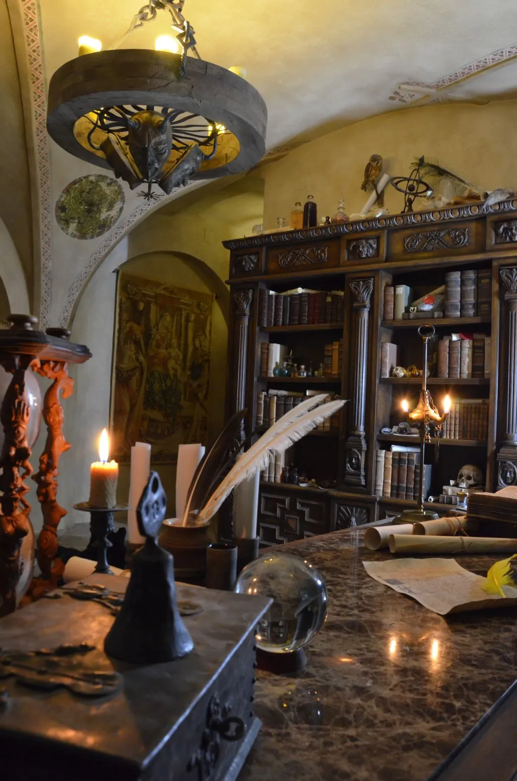 Interior of a Renaissance alchemical laboratory with a stone table, quill, candle, bookshelf, and ornate chandelier.