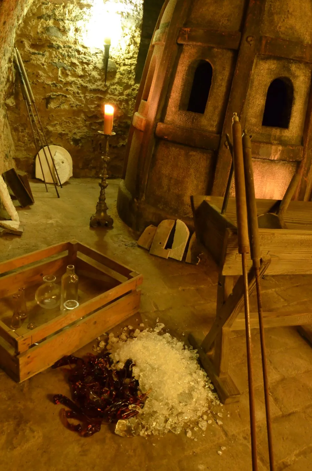 stone-walled room with wooden equipment, glass bottles, and a candlelit candelabra