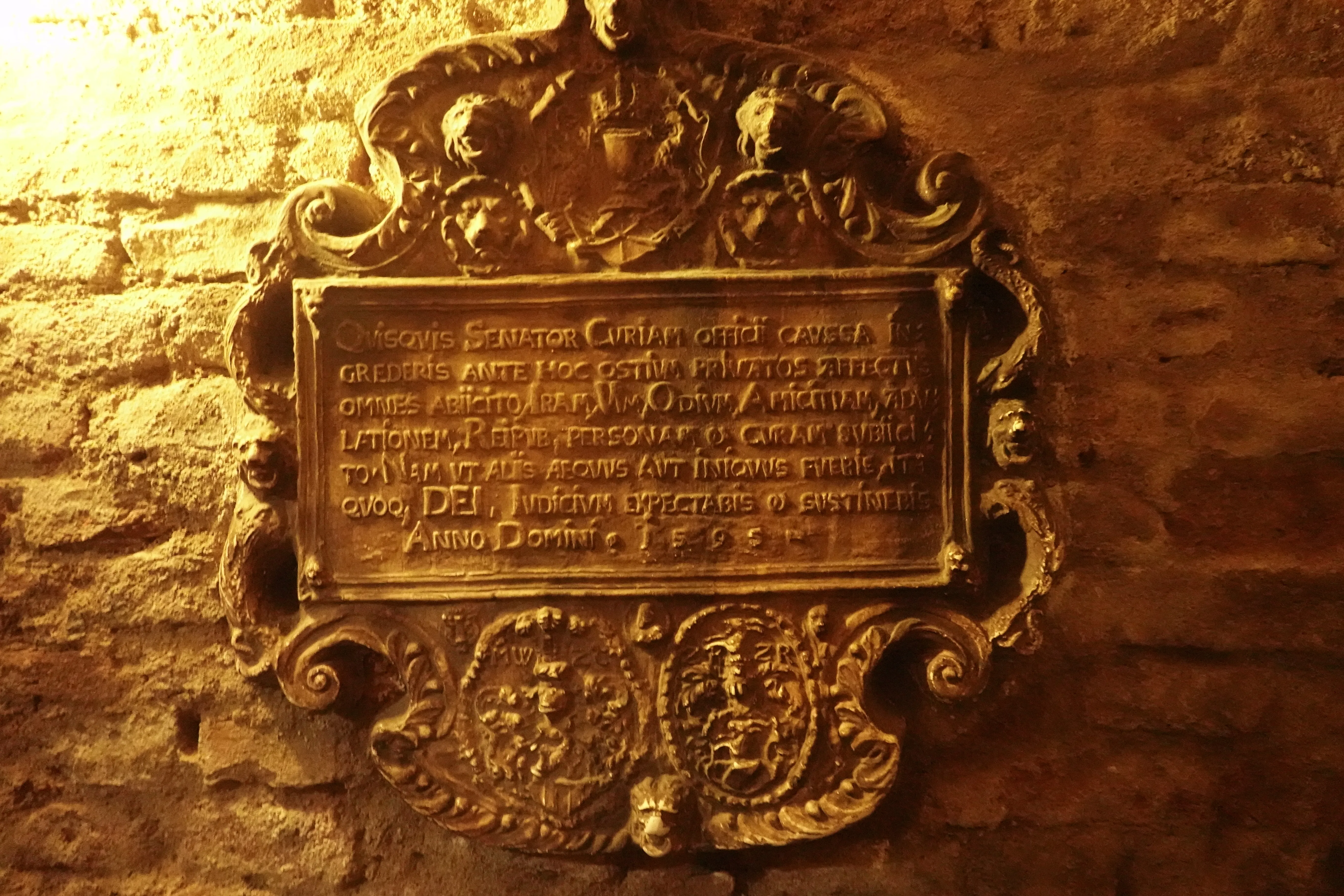 Gilded ornate plaque with Latin text mounted on a stone wall