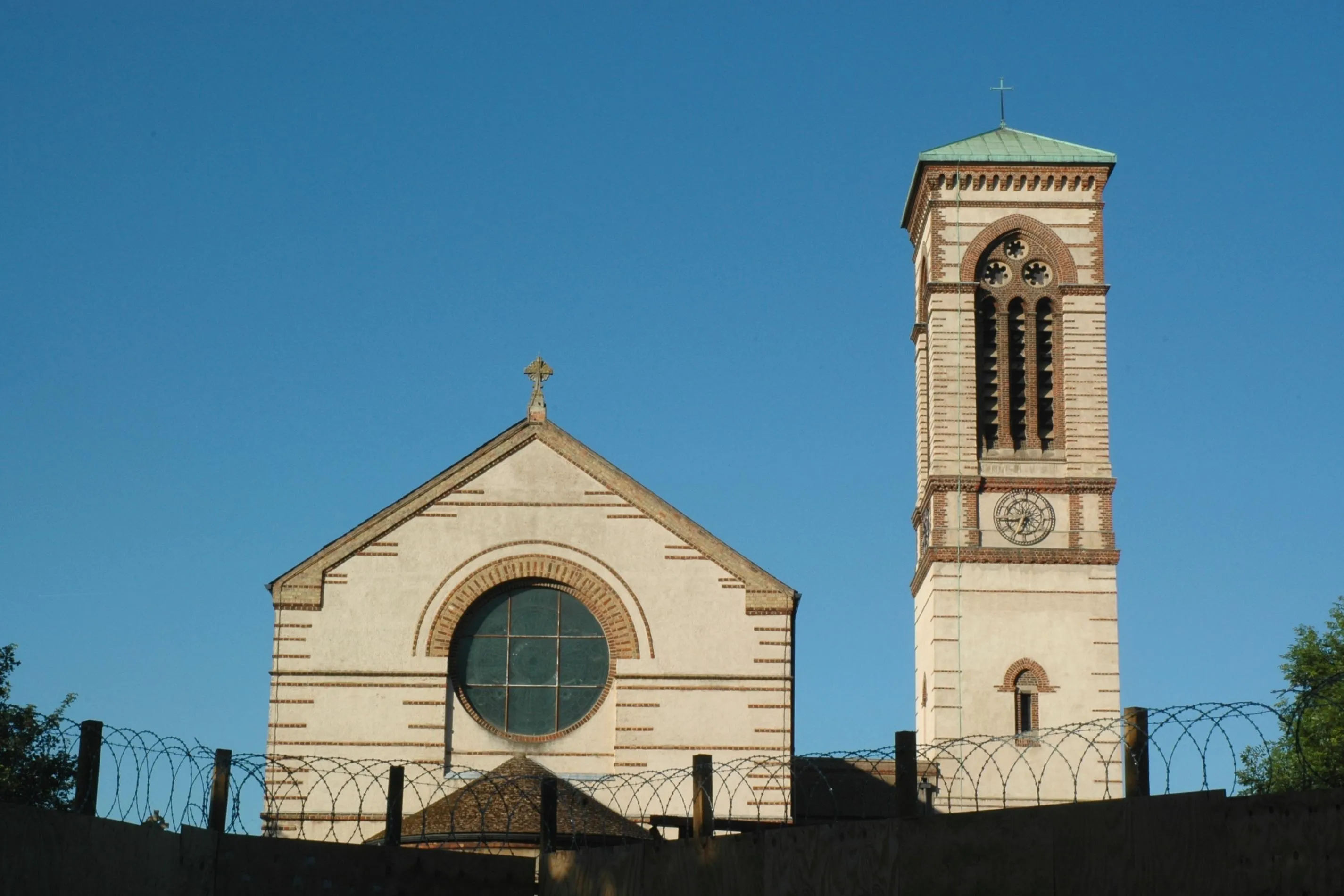 Fasada St Barnabas Church w stylu włoskiego romanizmu z dużym oknem rozetowym i wysoką dzwonnicą campanile na tle bezchmurnego błękitnego nieba