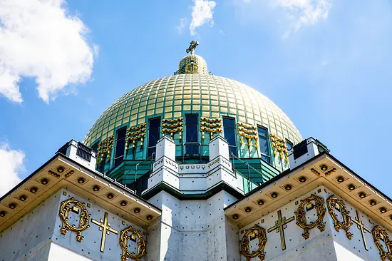 Cúpula verde de la Iglesia de San Carlos con cruces doradas y fachada de piedra blanca bajo un cielo azul