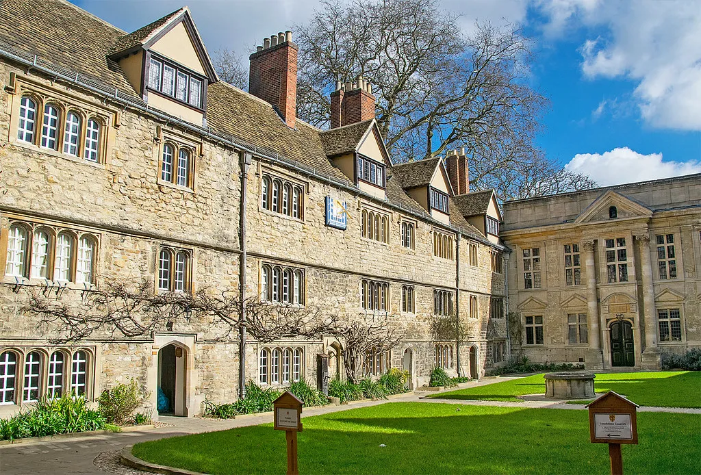 Edificios universitarios de piedra que rodean un patio con césped en St Edmund Hall, Oxford, con cielo azul y árboles sin hojas