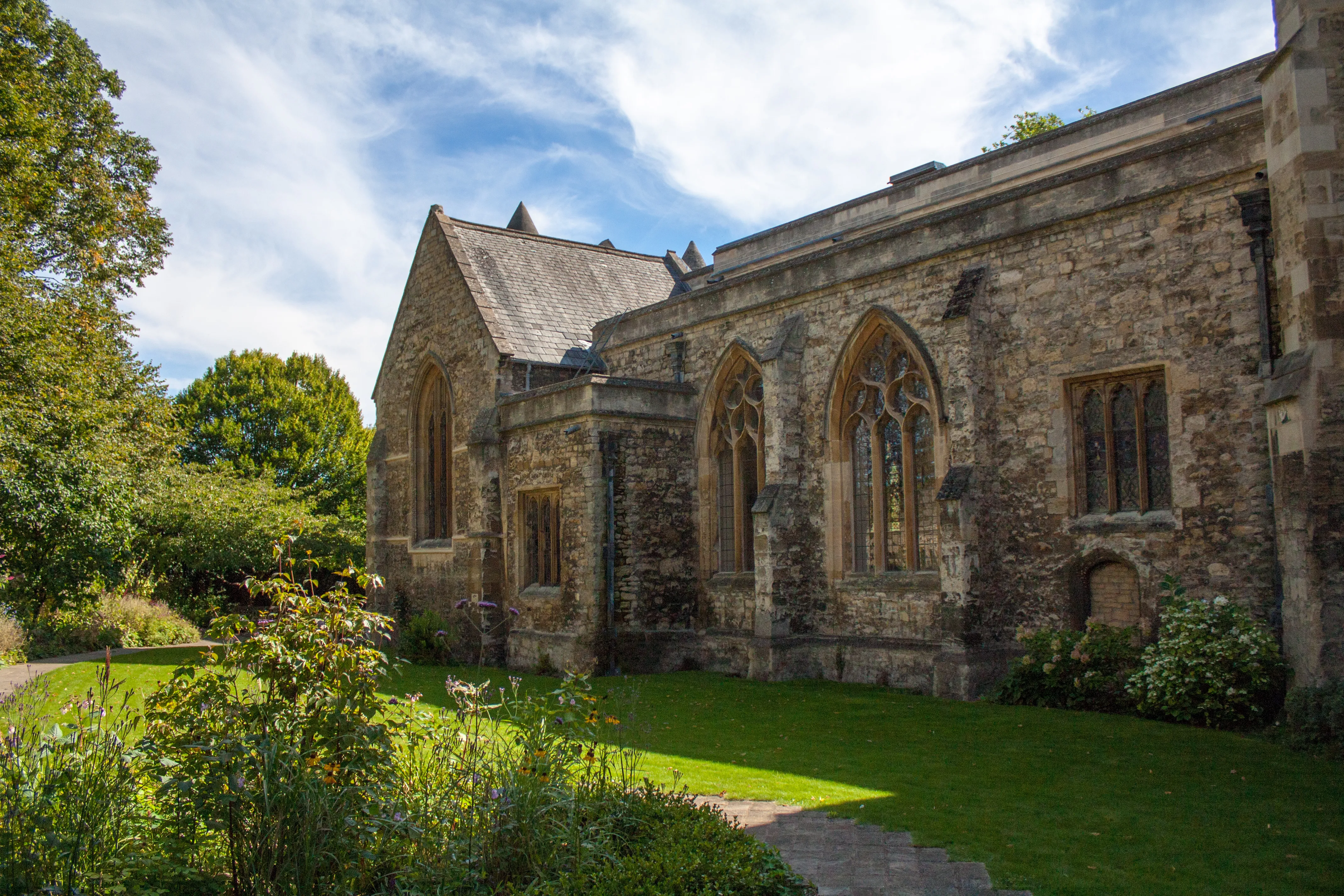 Edificio de piedra de estilo gótico con ventanas arqueadas rodeado por un césped verde y árboles en St Edmund Hall, Oxford