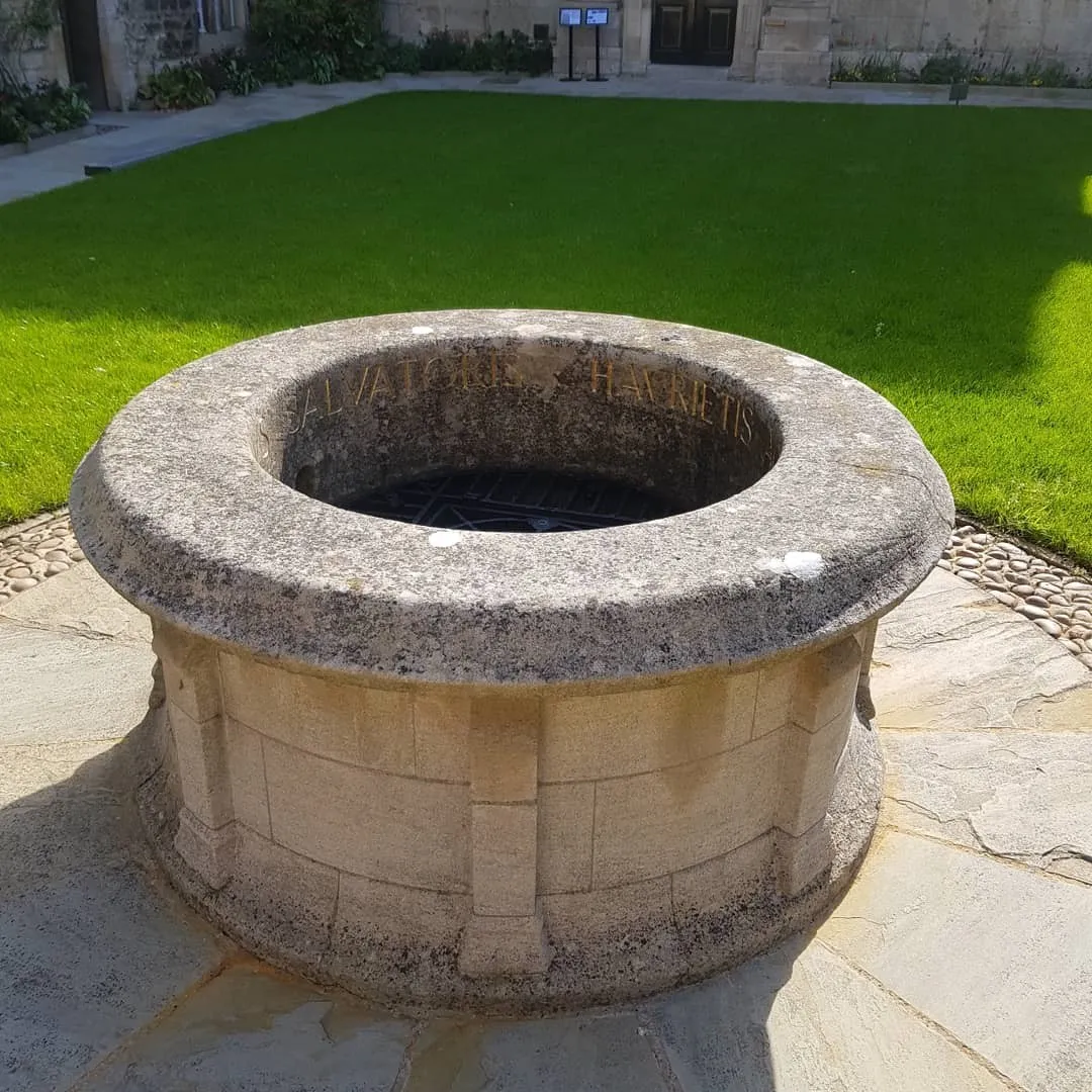Pozo circular de piedra en el patio ajardinado de St Edmund Hall, Oxford, con edificios de piedra visibles al fondo