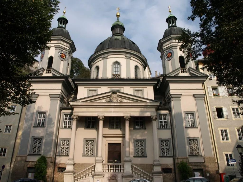Baroque facade of St. Erhard's Church with a central dome flanked by two green-domed bell towers and a columned entrance portico