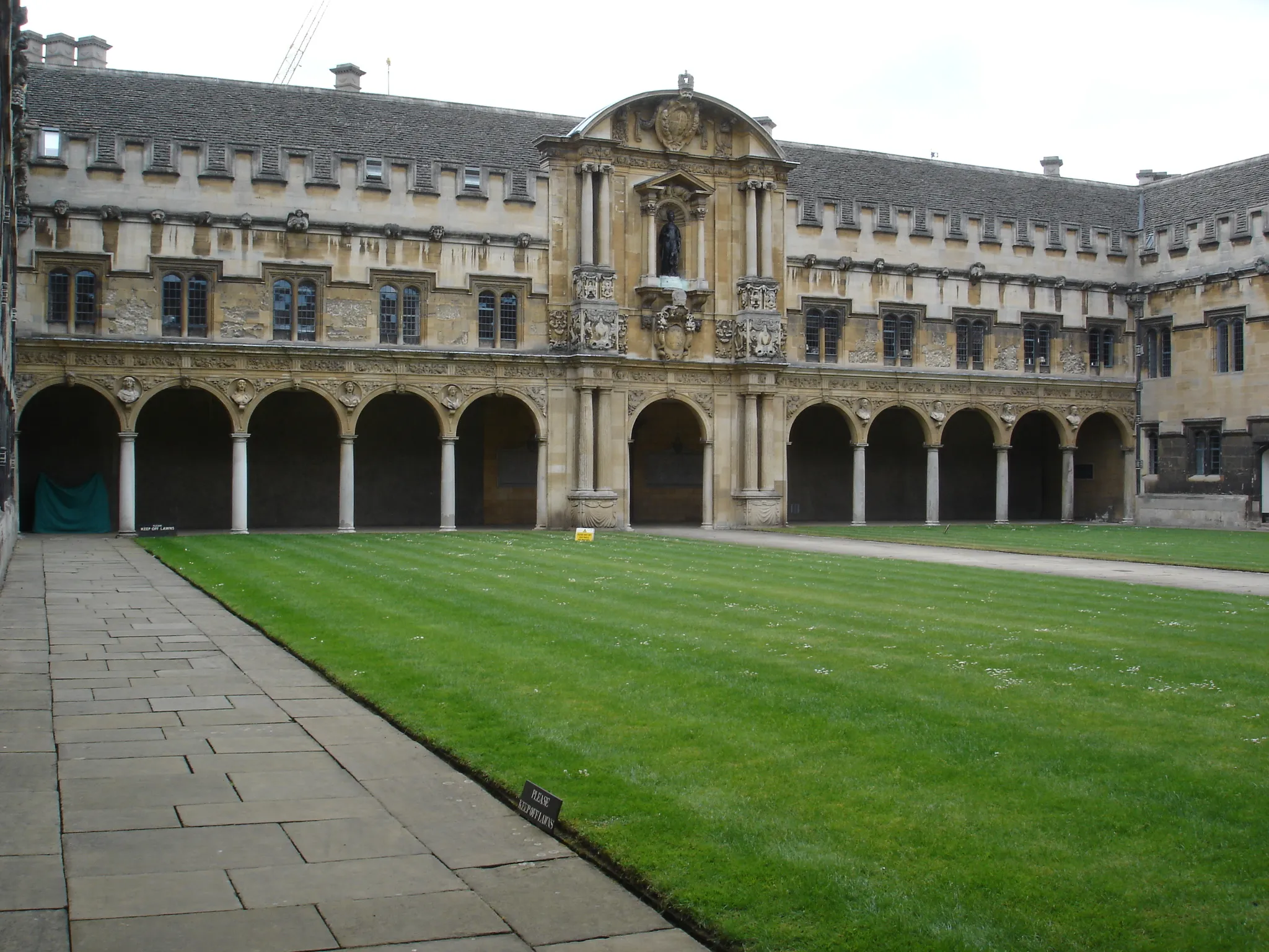 Historische 'college quadrangle' met een groot groen gazon, omzoomd door stenen arcadegangen en een sierlijke centrale toegangspoort.