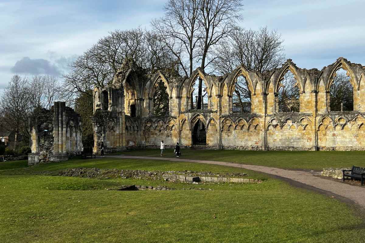 Stenen ruïnes van St Mary's Abbey met gotische bogen en muren, een groen gazon en een pad op de voorgrond, kale bomen op de achtergrond