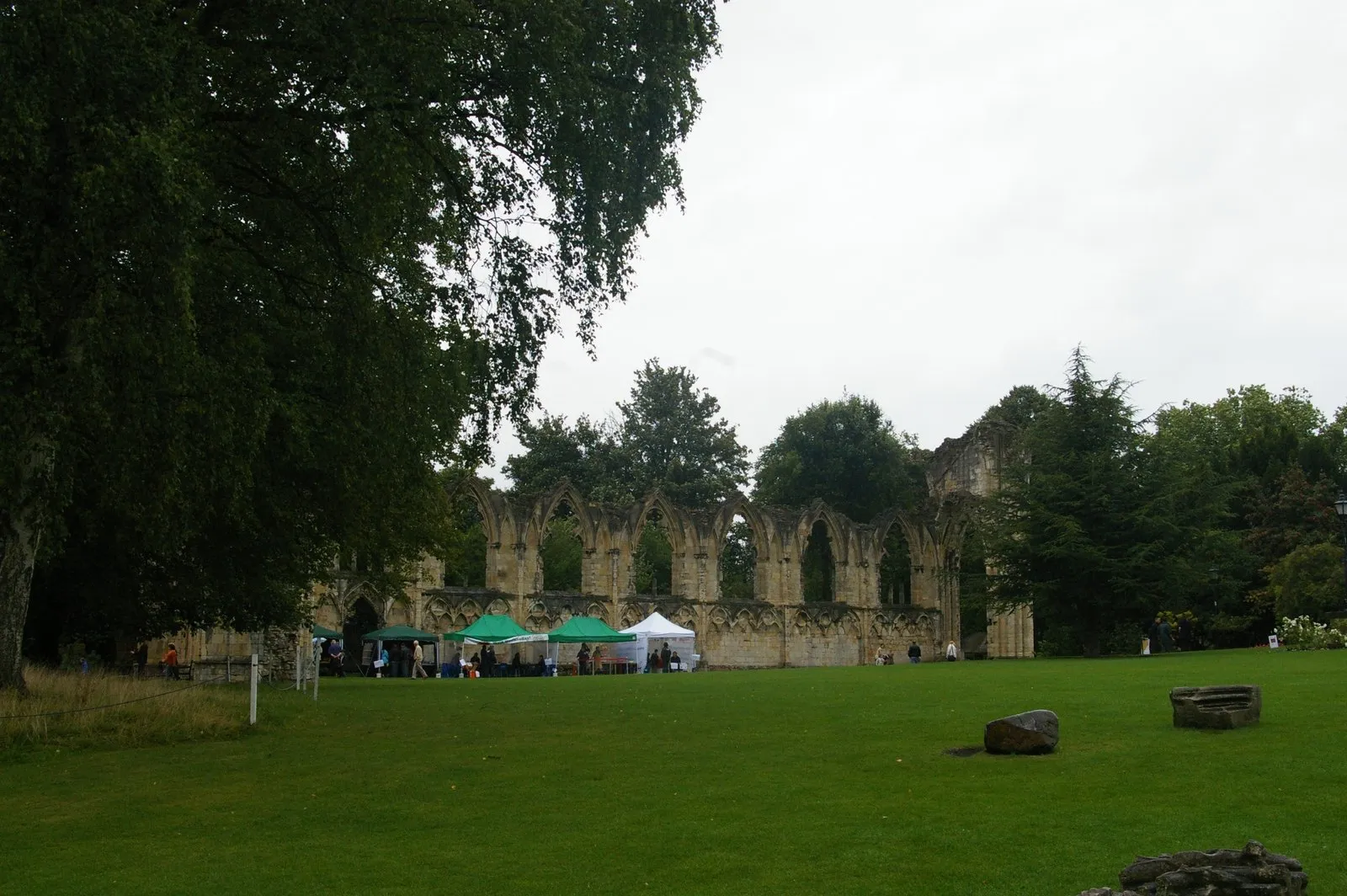Stenen ruïnes van St Mary's Abbey met hoge boogramen en muren, omringd door bomen en een groen gazon met evenementententen ervoor opgesteld