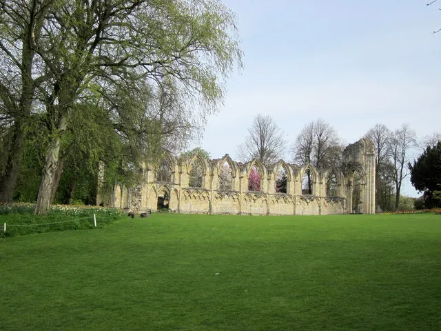 Stenen ruïnes van St Mary's Abbey met boogvensters, gelegen achter een groen gazon en grote bomen.