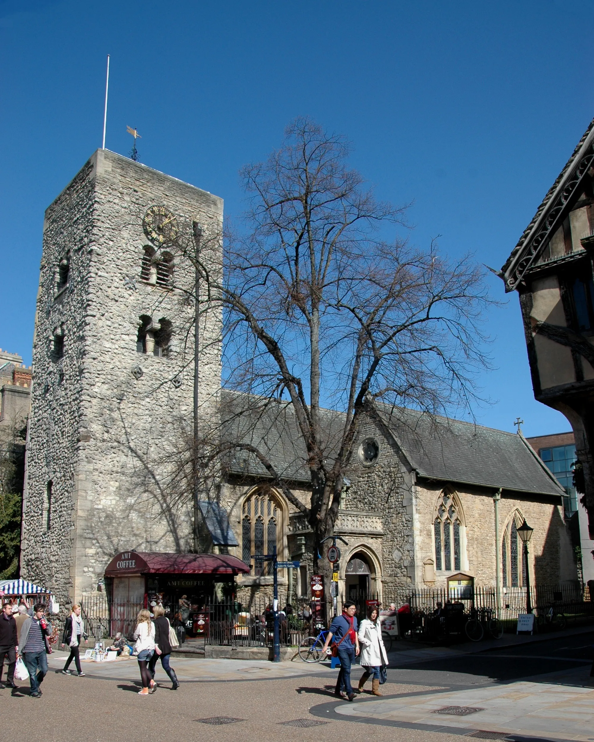 Stenen Saksische toren en kerkgebouw van St Michael at the North Gate in Oxford, met voetgangers op de bestrate straat ervoor
