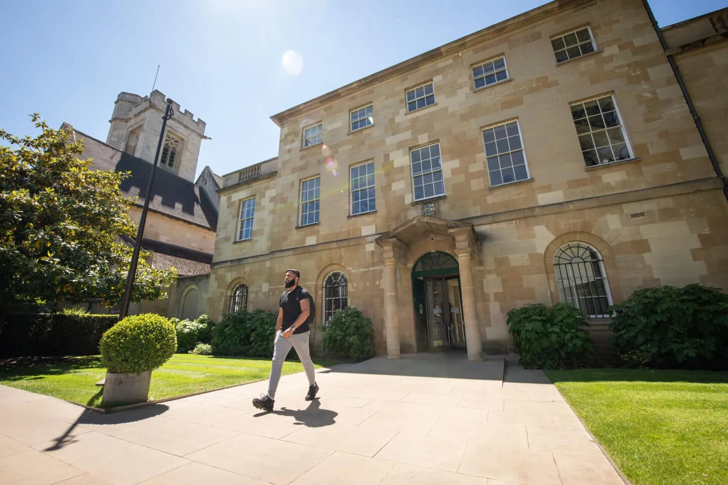 Man loopt over een binnenplaats voor een historisch stenen universiteitsgebouw met een kerktoren op de achtergrond