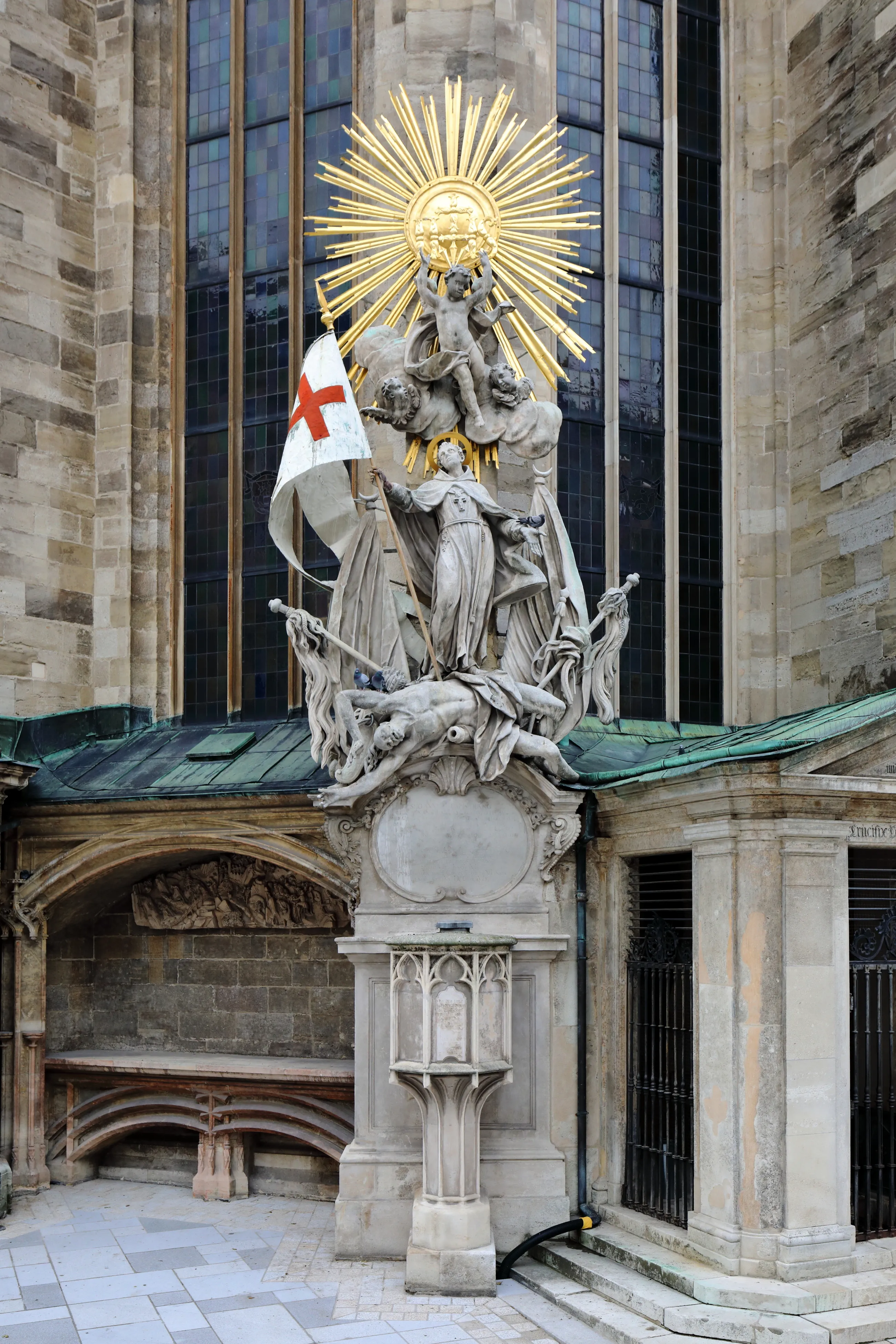 A large ornate stone and gold sculpture with religious figures and a sunburst, set against the stone facade and tall windows of a Gothic cathedral.