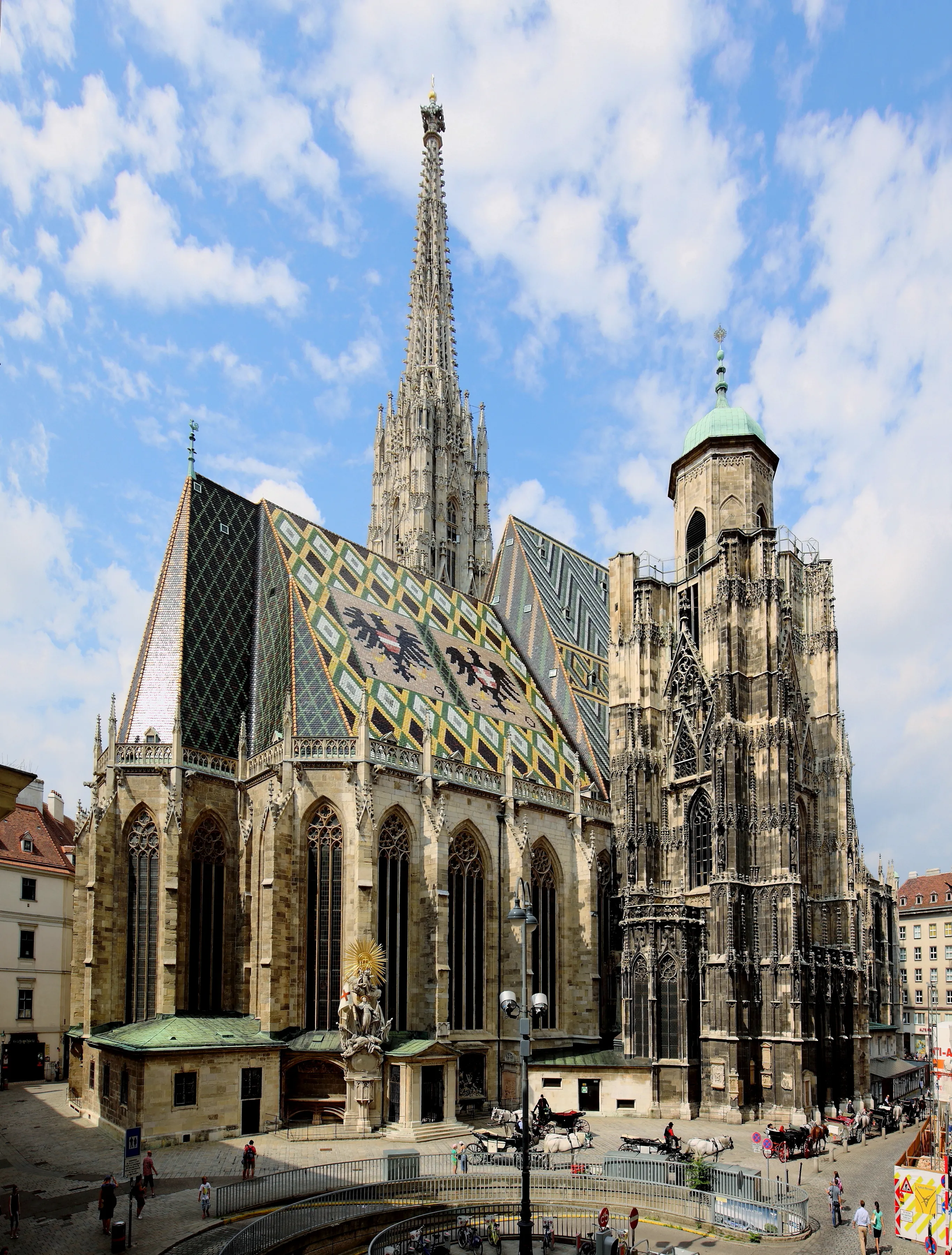 St. Stephen's Cathedral with a colorful tiled roof and tall spire under a blue sky with clouds